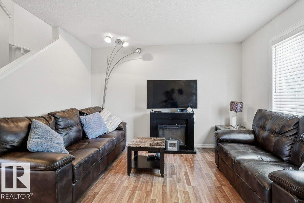 Living area featuring wood-finish flooring, a contemporary fireplace, and crisp white walls - 30 1404 Hermitage Road, Edmonton, AB