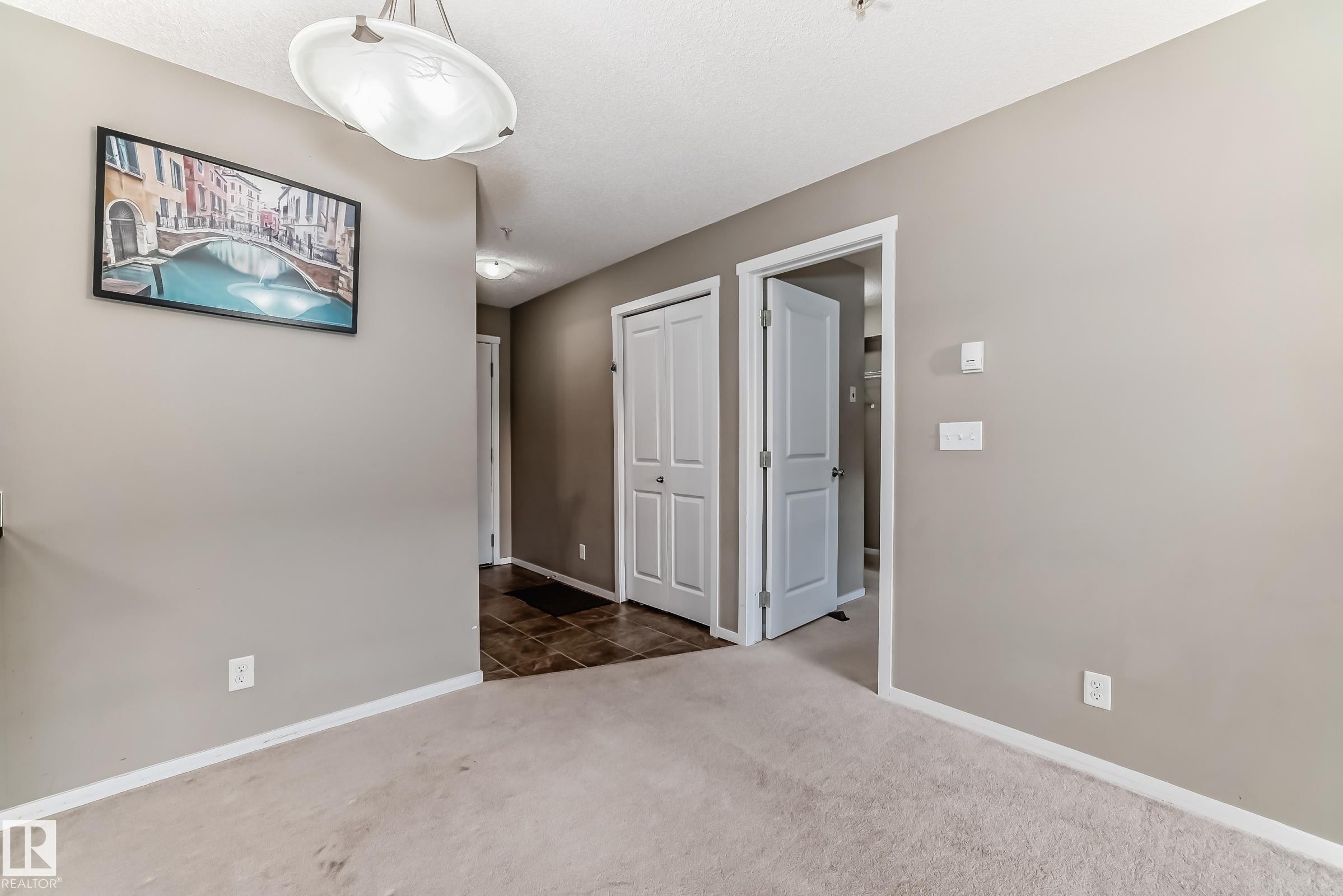 Carpeted flooring extending into a hallway with contrasting dark tile - #121 111 Watt Cm Sw, Edmonton, AB - Indoor Photo Showing Other Room