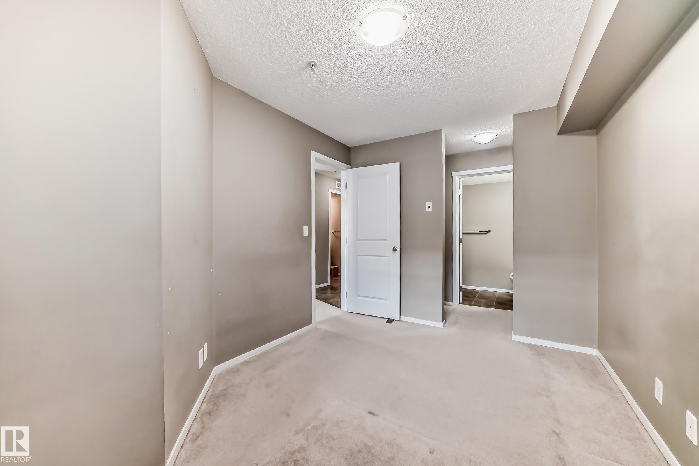 Carpeted room featuring a neutral paint palette, two interior doors, and overhead flush mount lighting - #121 111 Watt Cm Sw, Edmonton, AB - Indoor Photo Showing Other Room
