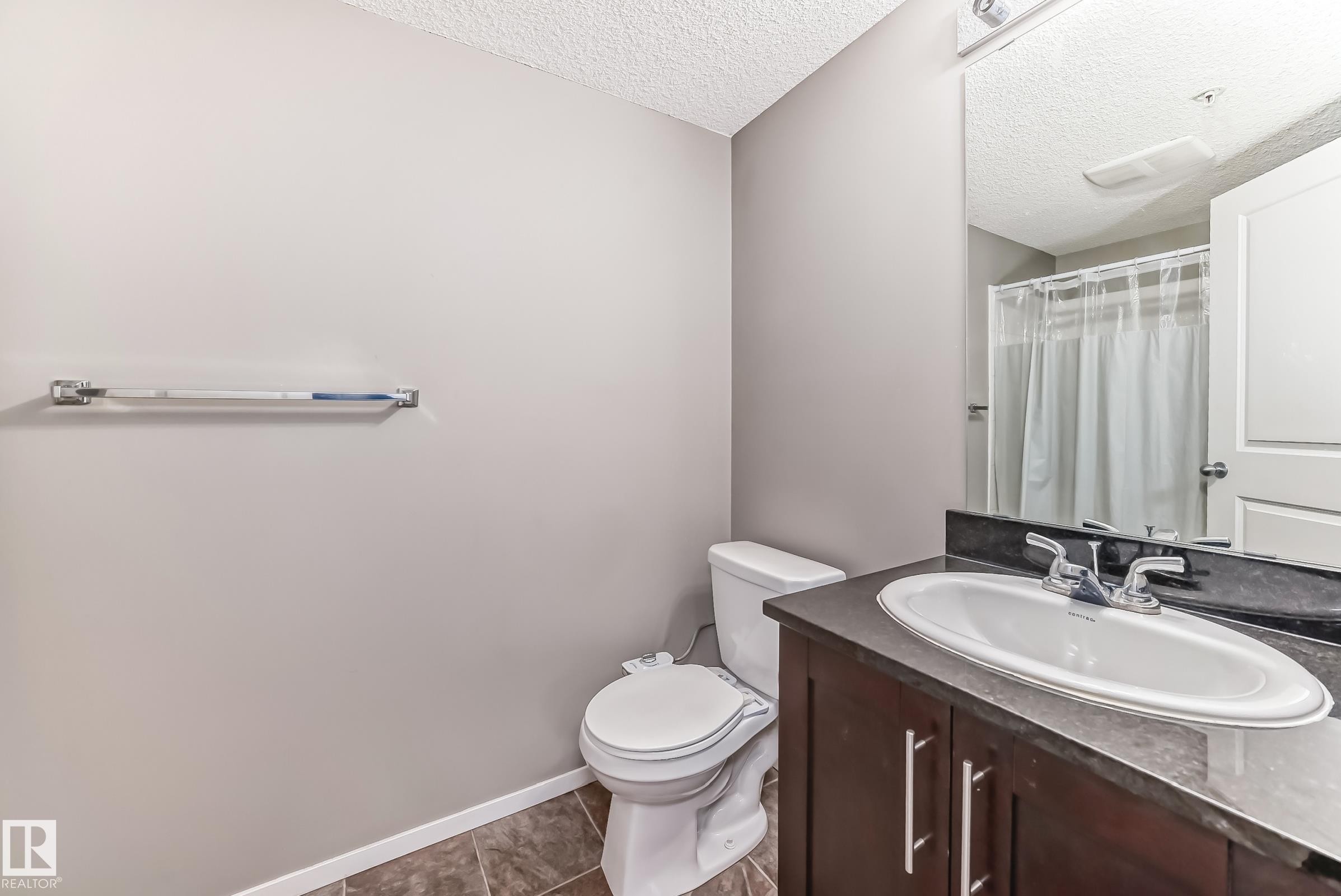 Bathroom featuring a dark wood-finish vanity with a white oval sink, dark countertop, and chrome faucet - #121 111 Watt Cm Sw, Edmonton, AB - Indoor Photo Showing Bathroom