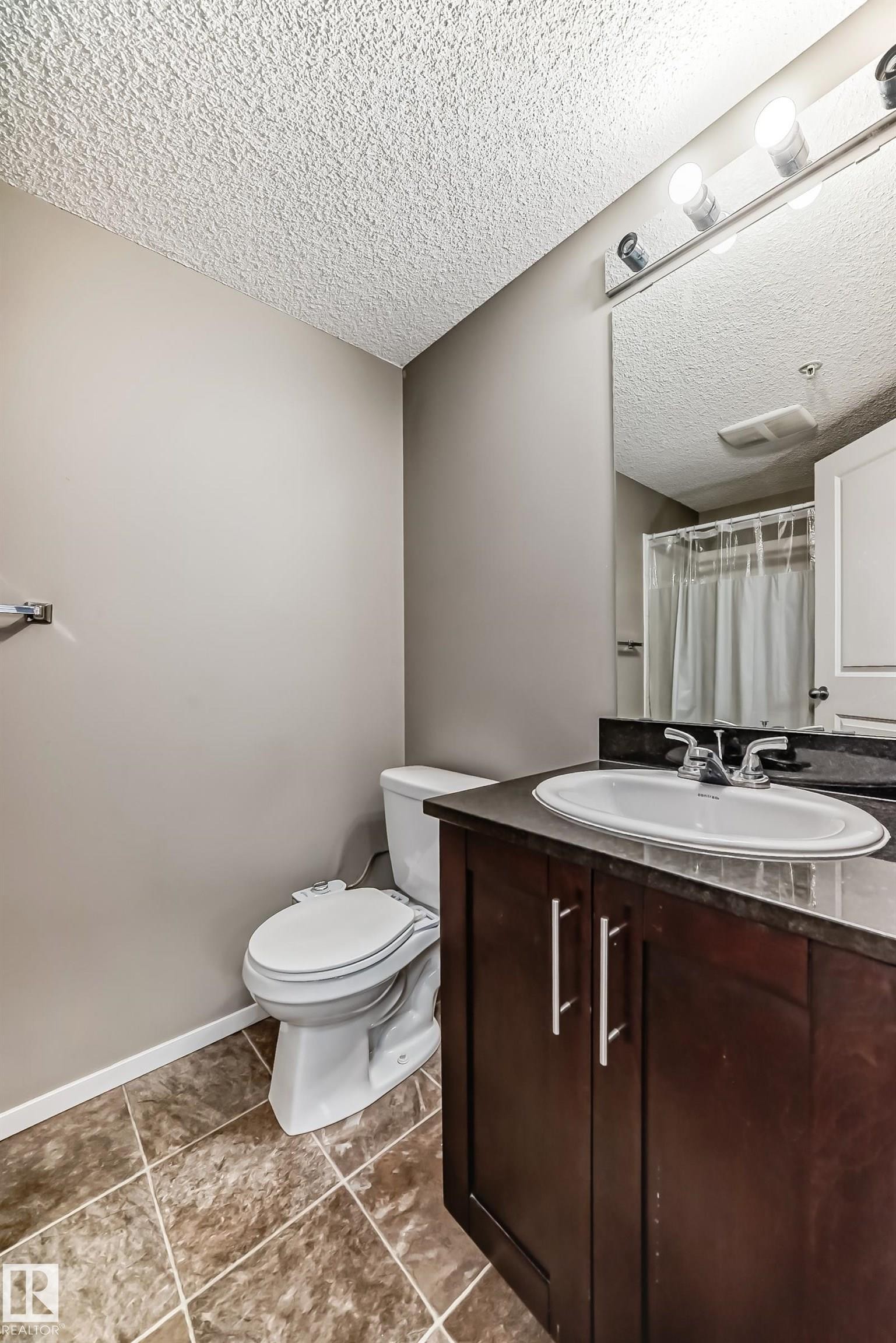 Bathroom vanity with dark wood-finish cabinetry, an oval undermount sink, and a dark stone-look countertop - #121 111 Watt Cm Sw, Edmonton, AB - Indoor Photo Showing Bathroom