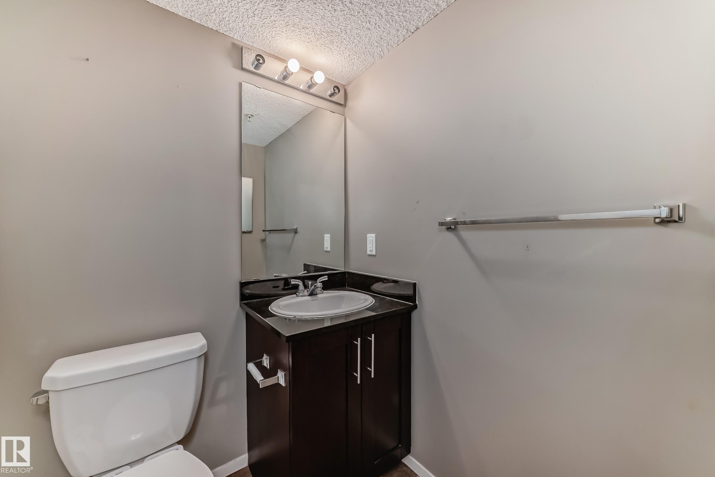 Bathroom featuring a dark wood-finish vanity with an integrated sink, dark countertop, and brushed nickel hardware - #121 111 Watt Cm Sw, Edmonton, AB - Indoor Photo Showing Bathroom