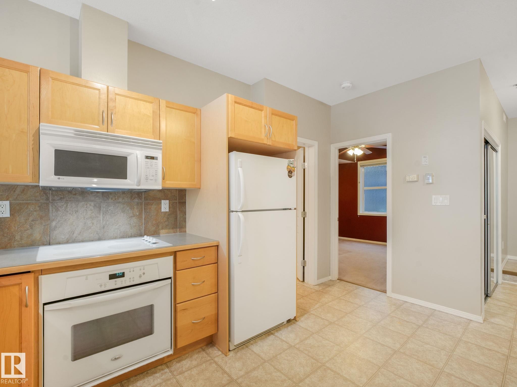 Kitchen area featuring light wood cabinetry, white appliances, and a tiled backsplash - 150 4827 104A Street, Edmonton, AB