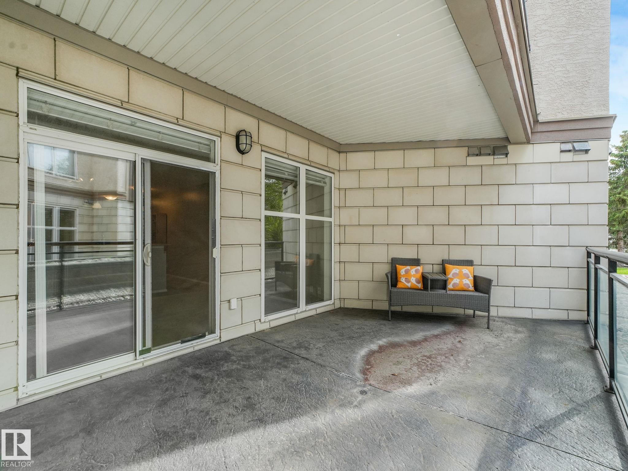 Private covered patio featuring a stamped concrete surface and glass panel railing - 150 4827 104A Street, Edmonton, AB