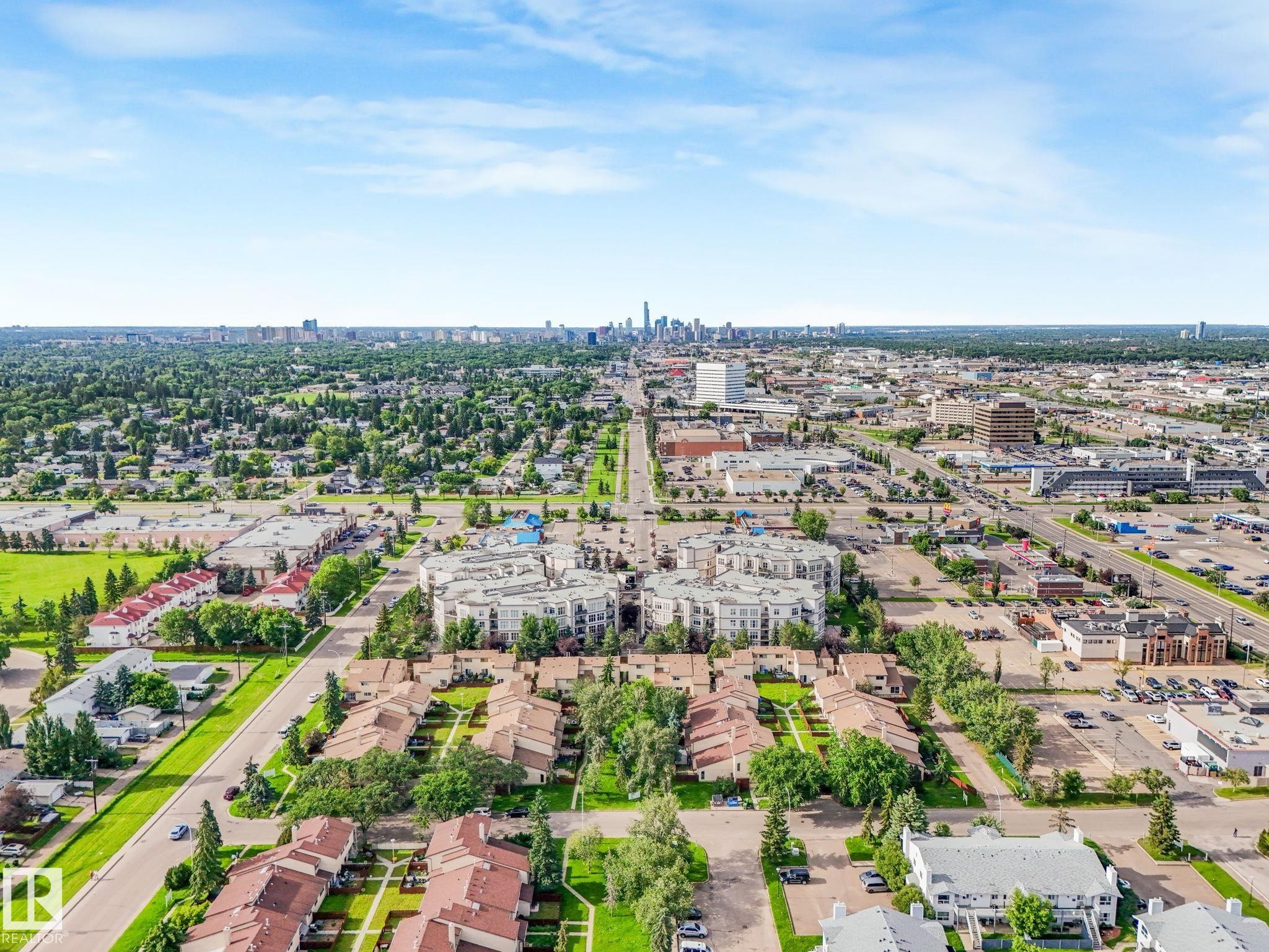 Aerial perspective showcasing a residential area with varied housing types, extensive green spaces, and a distant city skyline - 150 4827 104A Street, Edmonton, AB