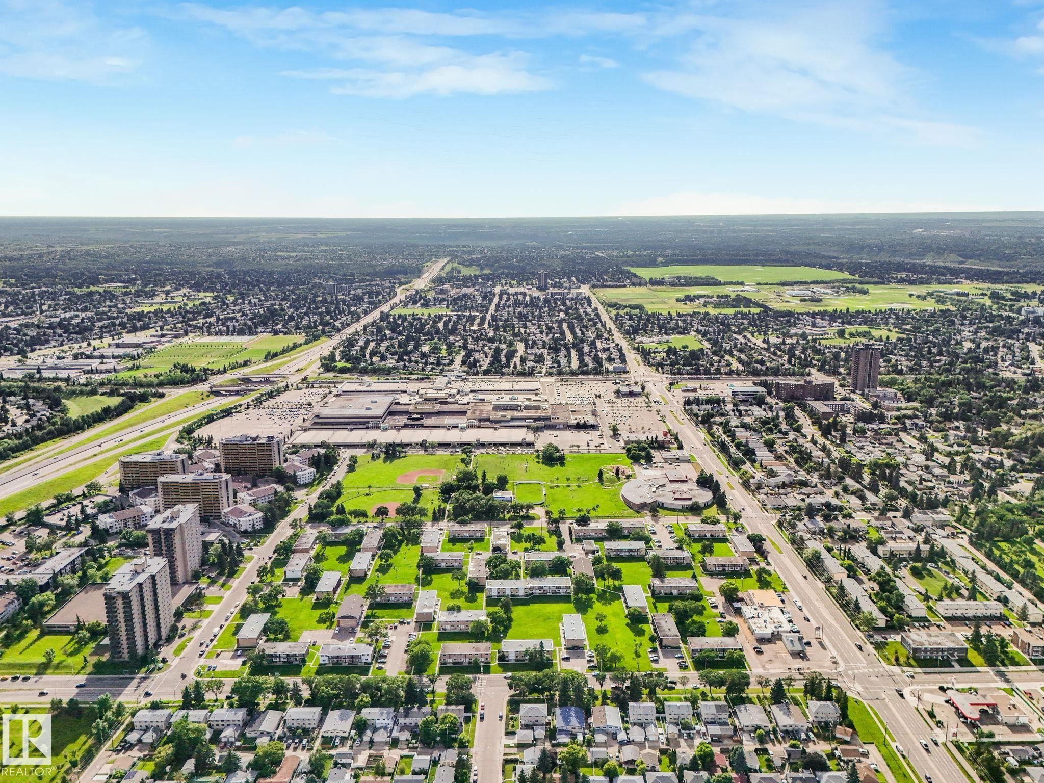 Aerial perspective showcasing a mixed-use district with low-rise and high-rise residential buildings, commercial structures, and extensive green spaces - 150 4827 104A Street, Edmonton, AB