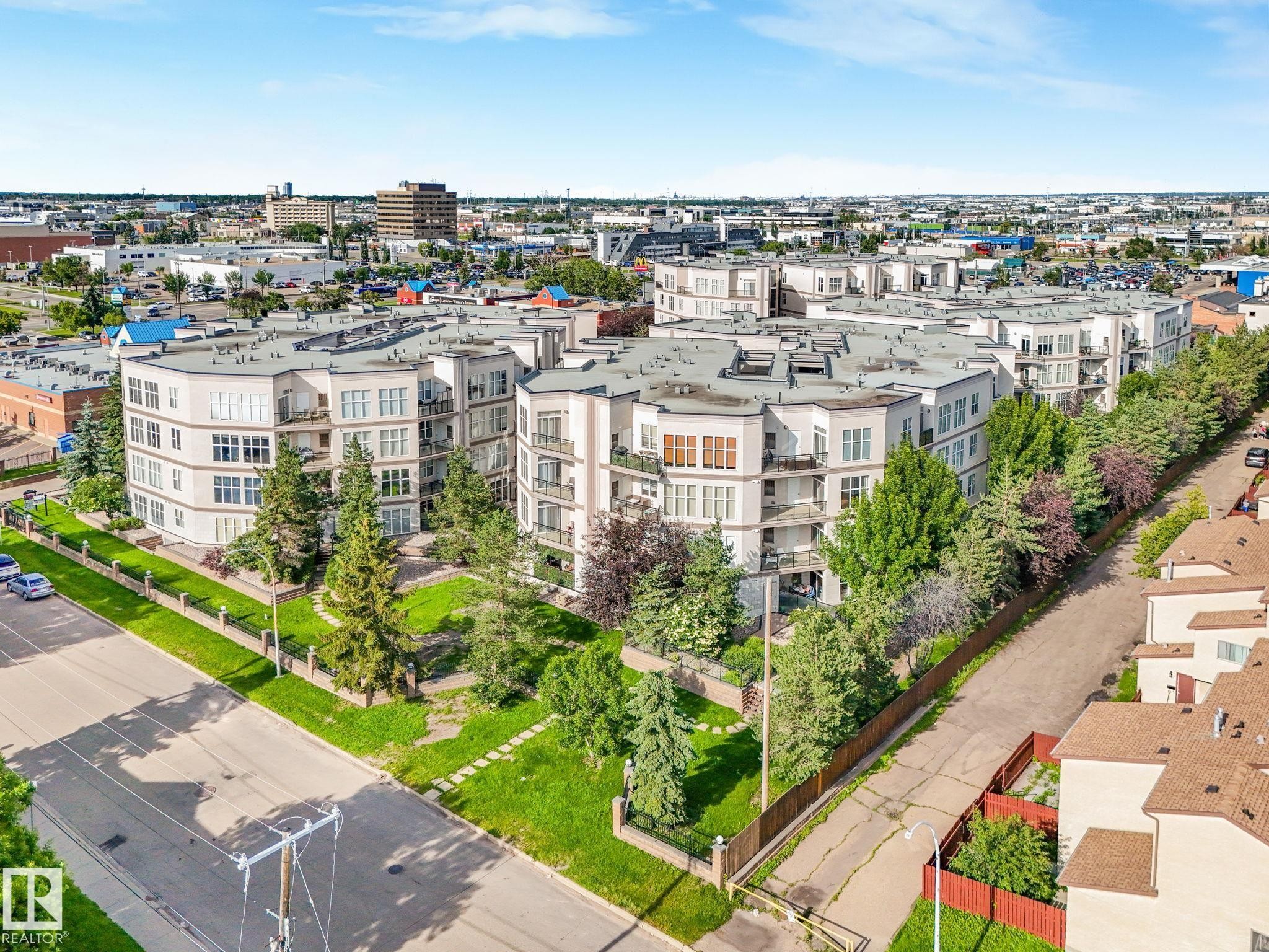 Multi-story residential buildings featuring contemporary architecture with numerous balconies, perimeter landscaping, and a surrounding urban environment - 150 4827 104A Street, Edmonton, AB