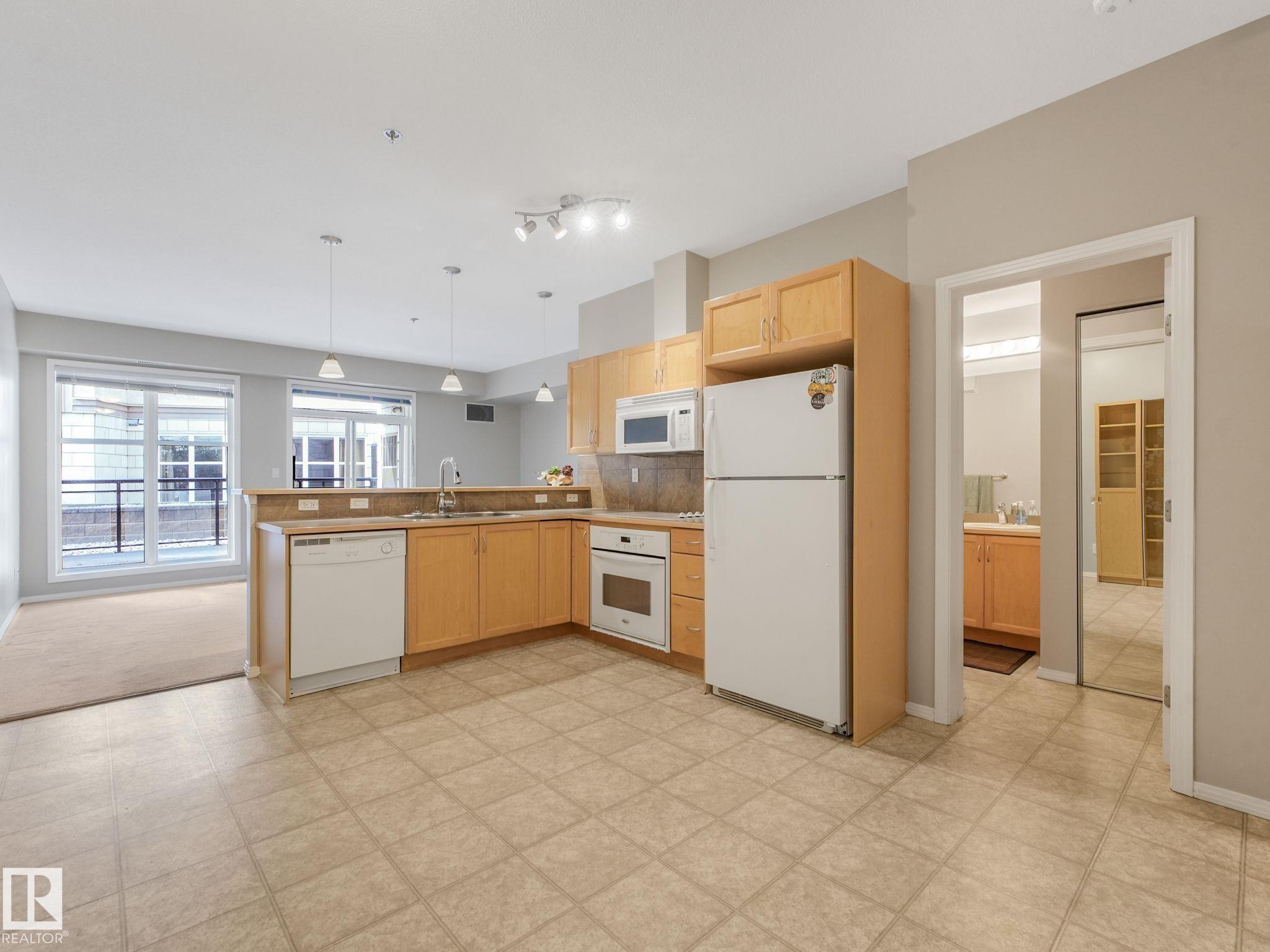 Open-concept kitchen featuring light wood cabinetry, a built-in microwave, integrated dishwasher, and tile flooring - 150 4827 104A Street, Edmonton, AB