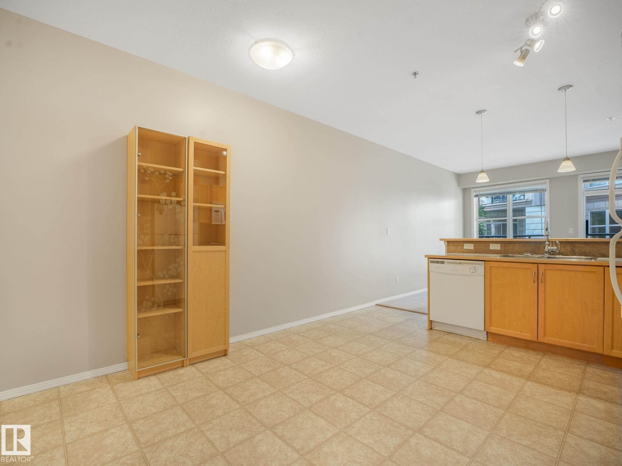 Kitchen area featuring light wood-finish cabinetry, a double basin sink, and an integrated white dishwasher - 150 4827 104A Street, Edmonton, AB