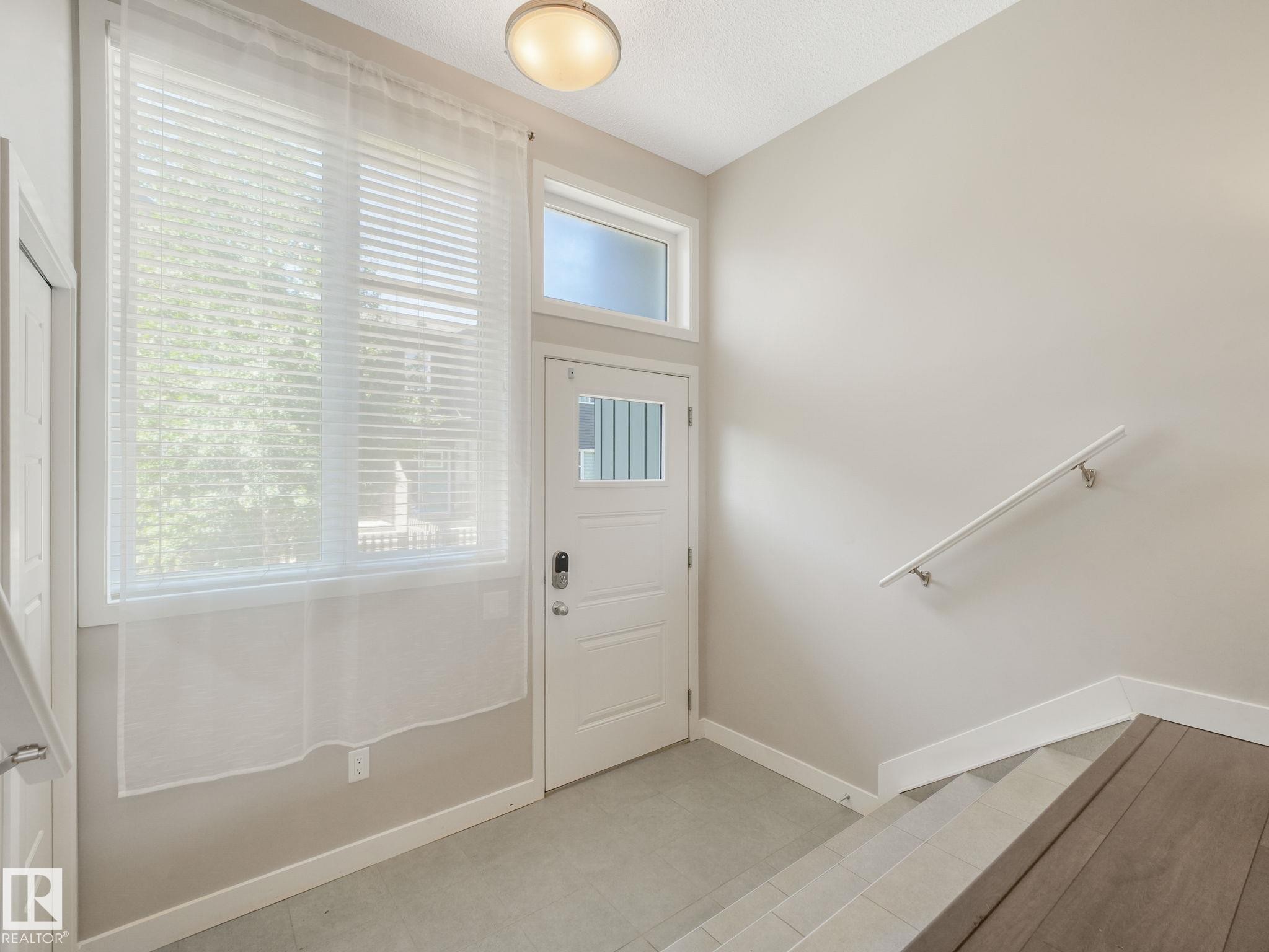 Entryway featuring a white paneled door with glass inserts, a transom window, and a large window with blinds - #55 4470 Prowse Rd Sw, Edmonton, AB - Indoor Photo Showing Other Room