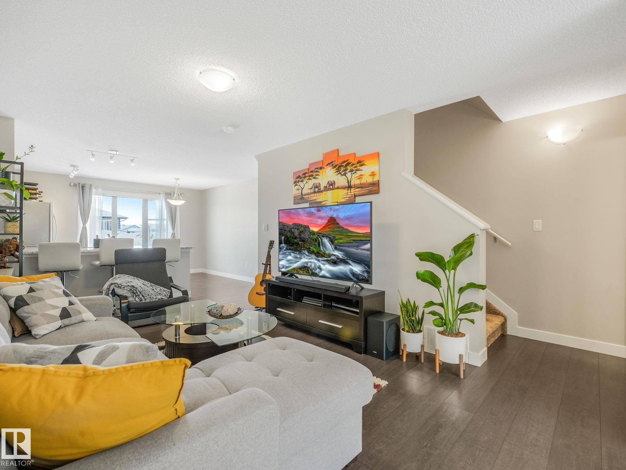 Open-concept living area featuring wood-finish flooring, a contemporary entertainment center, and a staircase with a white handrail - #55 4470 Prowse Rd Sw, Edmonton, AB - Indoor Photo Showing Living Room