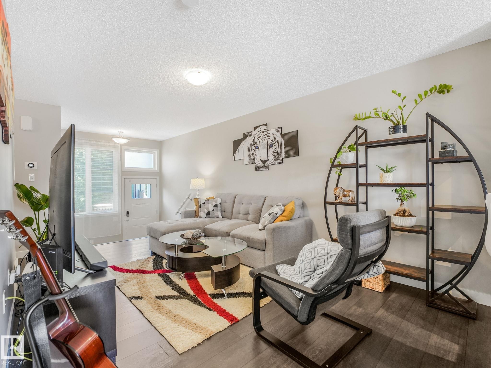 Spacious living area featuring wood-finish flooring, light grey wall tones, and a prominent front entry door with transom window - #55 4470 Prowse Rd Sw, Edmonton, AB - Indoor Photo Showing Living Room