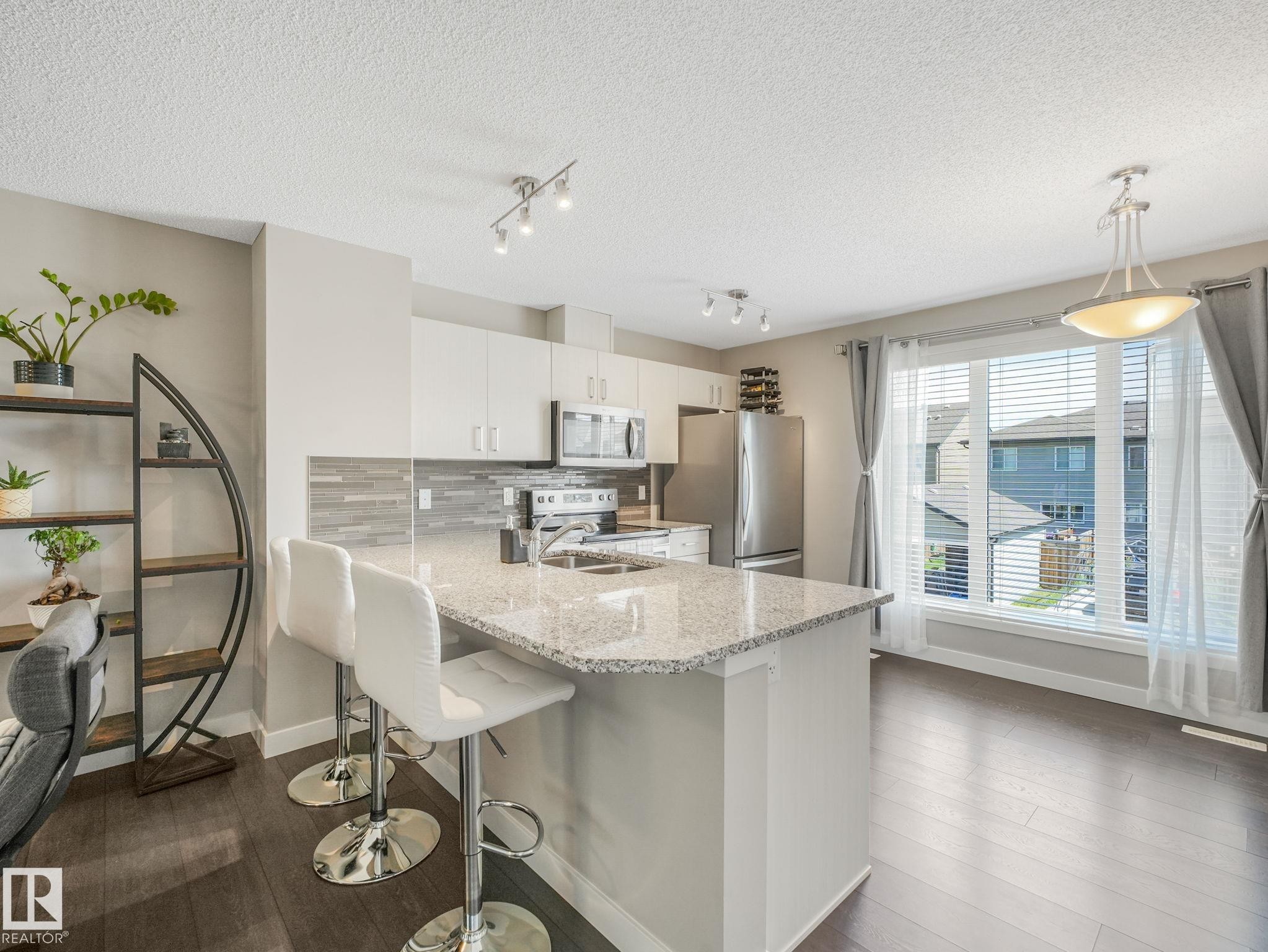 Kitchen island featuring a granite countertop with integrated sink and chrome faucet - #55 4470 Prowse Rd Sw, Edmonton, AB - Indoor Photo Showing Kitchen With Stainless Steel Kitchen With Double Sink With Upgraded Kitchen