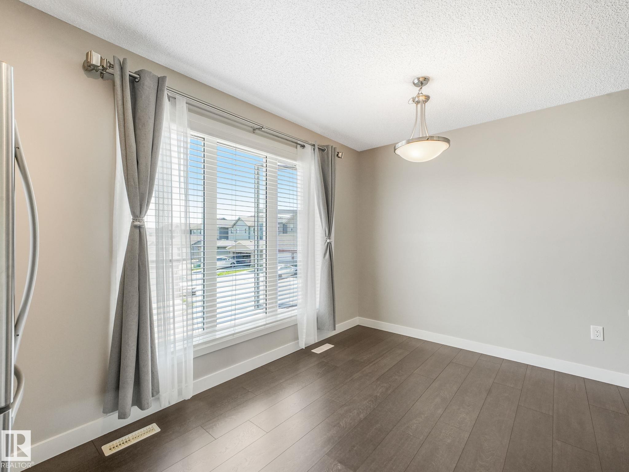 Bright room featuring a large window with blinds, wood-finish flooring, and a ceiling-mounted light fixture - #55 4470 Prowse Rd Sw, Edmonton, AB - Indoor Photo Showing Other Room