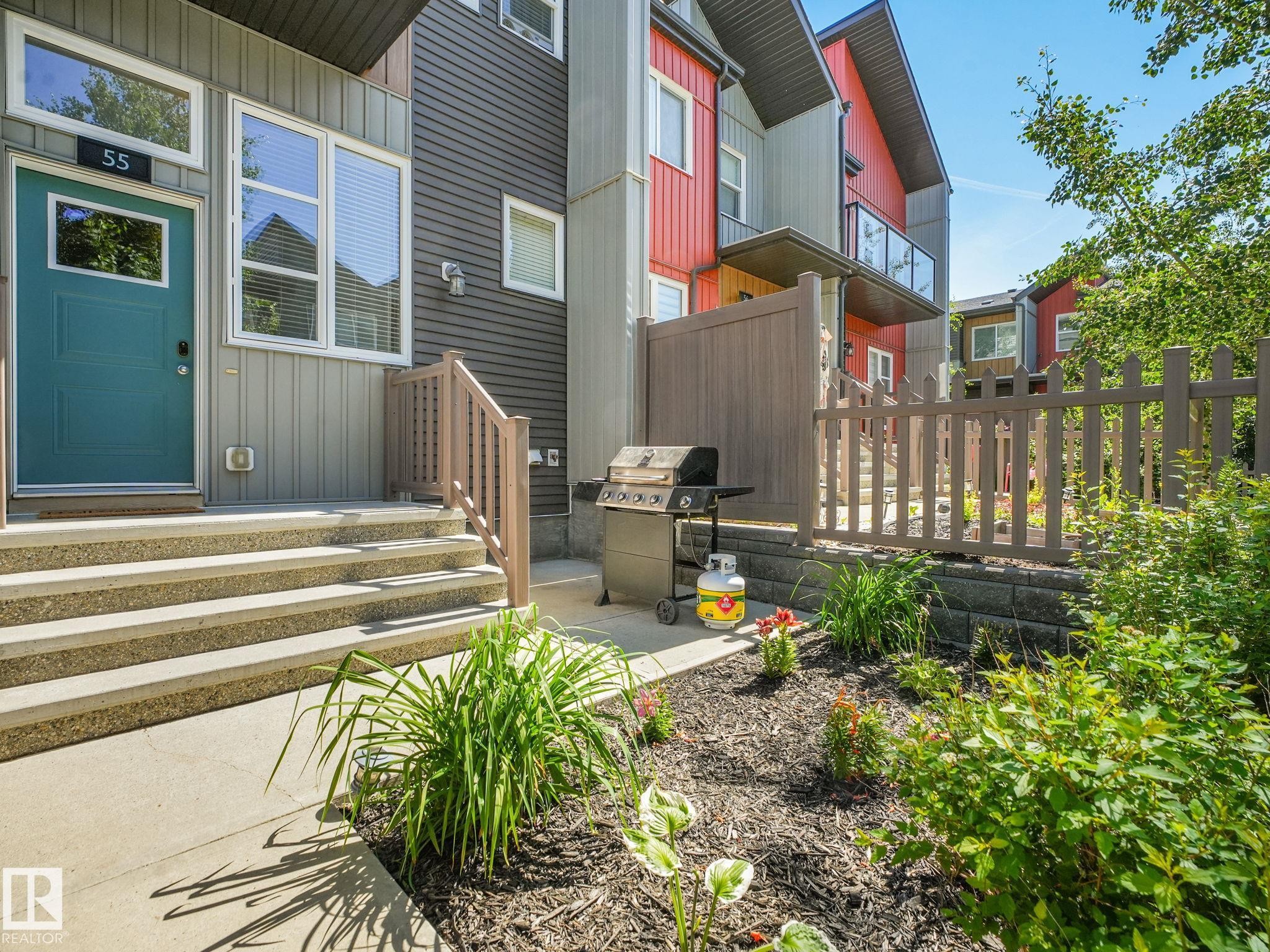 Modern townhouse exterior featuring a teal entry door, concrete steps, and a landscaped garden bed - #55 4470 Prowse Rd Sw, Edmonton, AB - Outdoor With Deck Patio Veranda