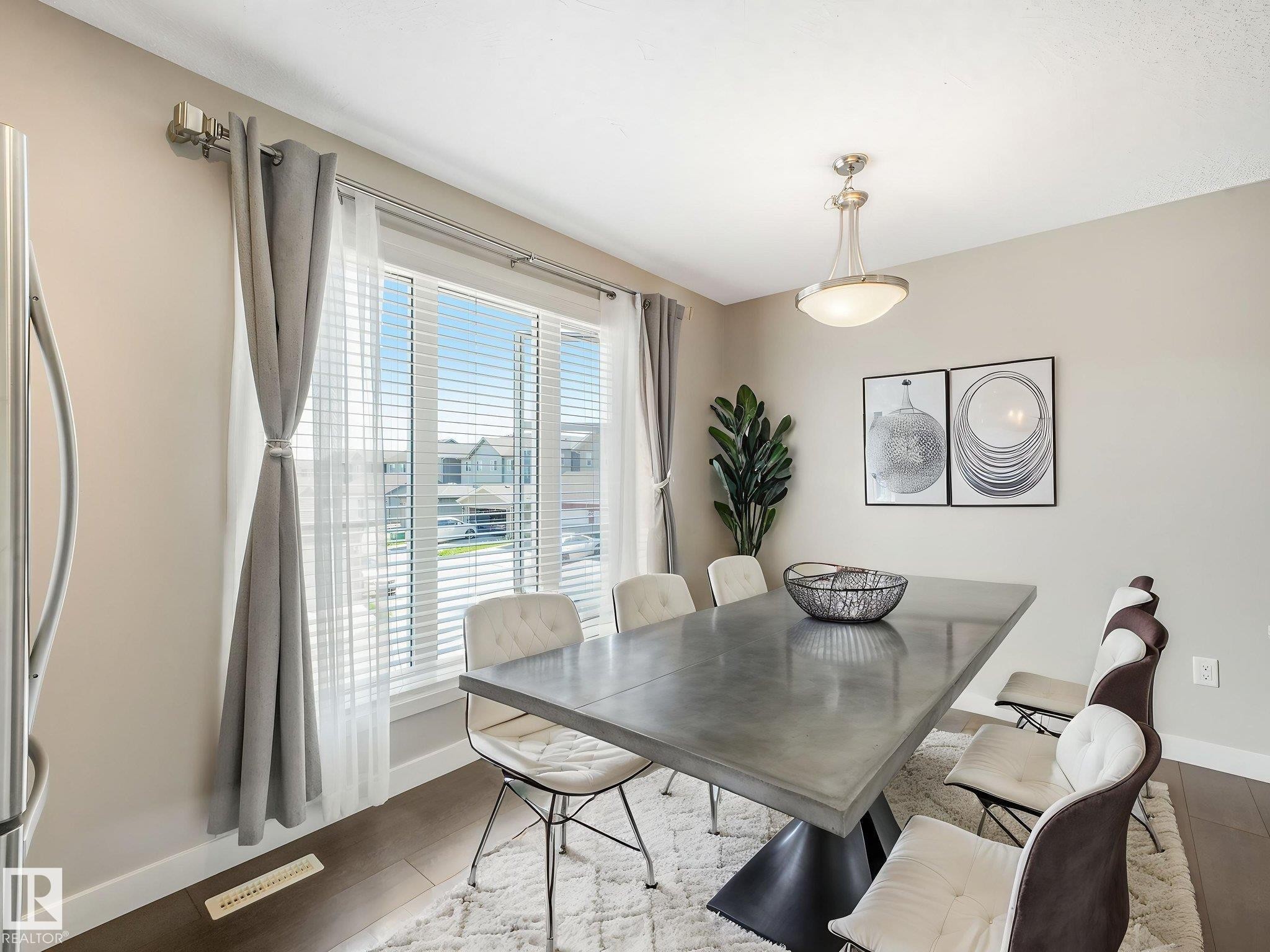 Spacious dining area featuring dark wood-finish flooring, a large window with white blinds, and a contemporary ceiling fixture - #55 4470 Prowse Rd Sw, Edmonton, AB - Indoor Photo Showing Dining Room