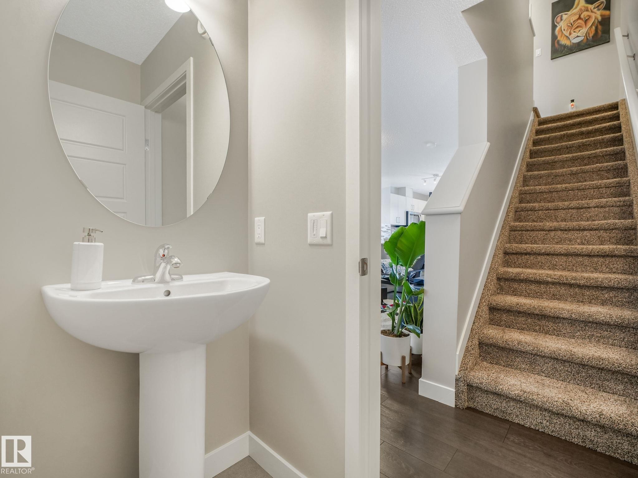Pedestal sink with chrome faucet, oval mirror, and a wall-mounted light fixture - #55 4470 Prowse Rd Sw, Edmonton, AB - Indoor Photo Showing Bathroom