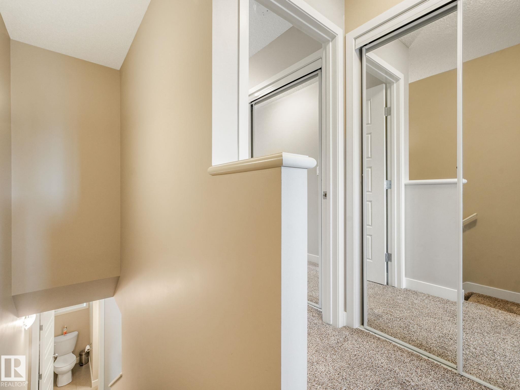 Hallway with mirrored closet doors, neutral carpet, and beige wall paint - #55 4470 Prowse Rd Sw, Edmonton, AB - Indoor Photo Showing Other Room