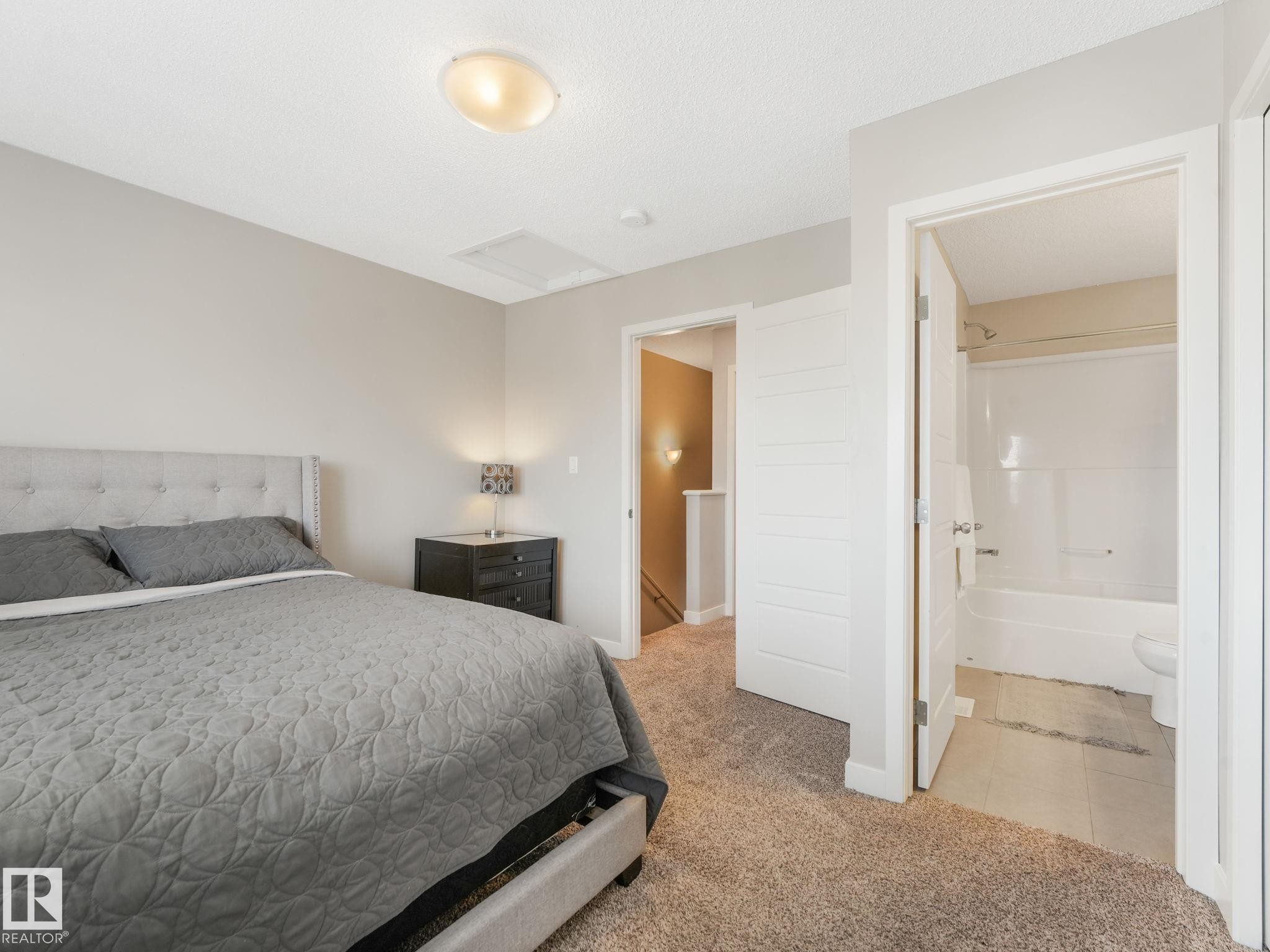 Carpeted bedroom featuring a textured ceiling, a flush-mount ceiling light, and access to a full bathroom with a tub/shower combination - #55 4470 Prowse Rd Sw, Edmonton, AB - Indoor Photo Showing Bedroom