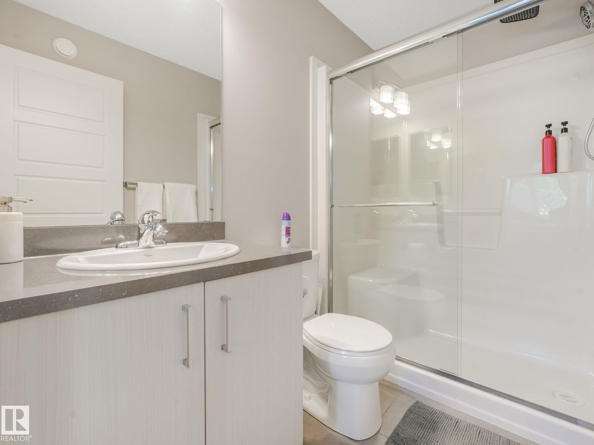 Bathroom featuring a white oval undermount sink, chrome faucet, grey countertop, and wood-finish vanity with handle pulls - #55 4470 Prowse Rd Sw, Edmonton, AB - Indoor Photo Showing Bathroom