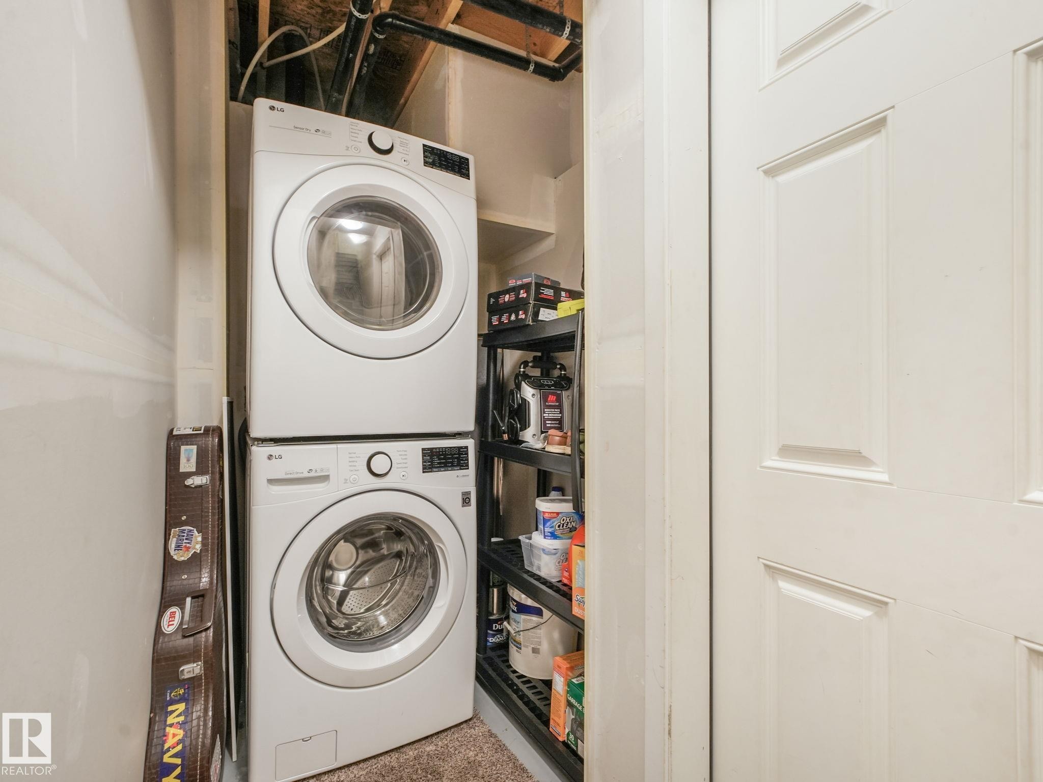 Dedicated laundry area featuring a stackable washer and dryer, adjacent built-in shelving, and a paneled white door - #55 4470 Prowse Rd Sw, Edmonton, AB - Indoor Photo Showing Laundry Room
