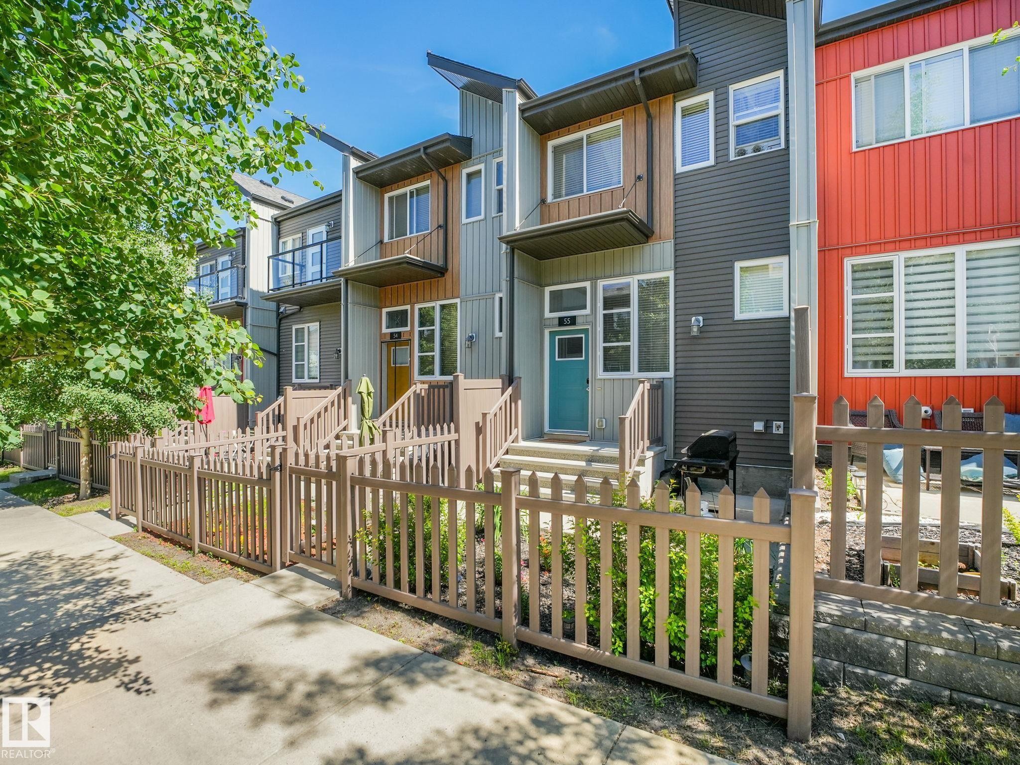 Modern townhome exterior featuring multi-toned siding, a teal entry door, and a private fenced front yard - #55 4470 Prowse Rd Sw, Edmonton, AB - Outdoor
