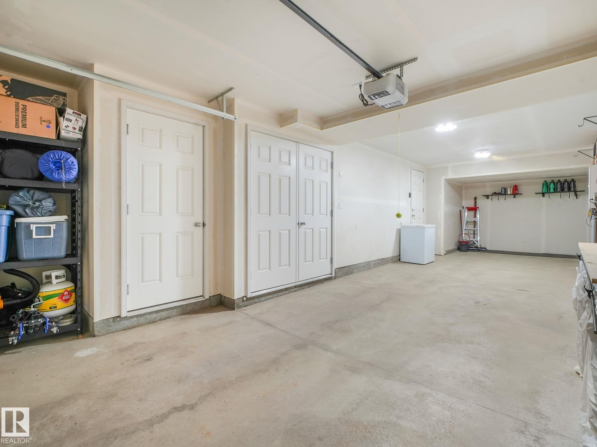 Spacious garage with multiple interior access doors and overhead lighting - #55 4470 Prowse Rd Sw, Edmonton, AB - Indoor Photo Showing Garage