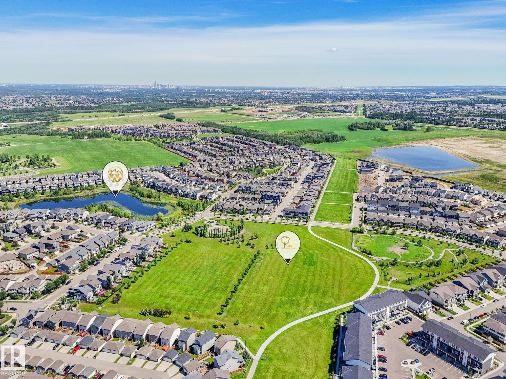 Aerial perspective showcasing a residential community with abundant green spaces, multiple residential structures, two distinct bodies of water, and surrounding undeveloped land - #55 4470 Prowse Rd Sw, Edmonton, AB - Outdoor With View
