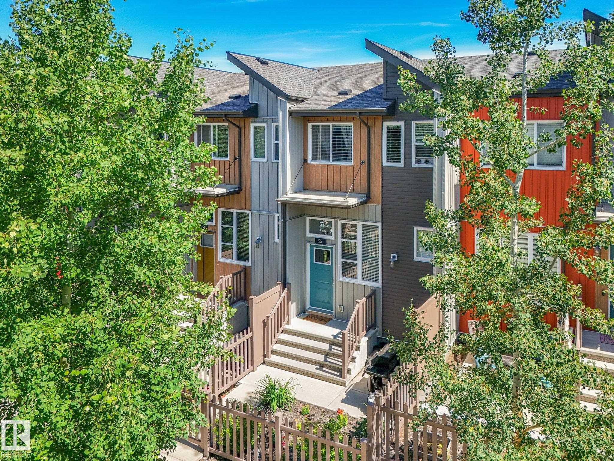 Modern townhome exterior featuring multi-toned siding, a teal entry door, and a private fenced front yard - #55 4470 Prowse Rd Sw, Edmonton, AB - Outdoor