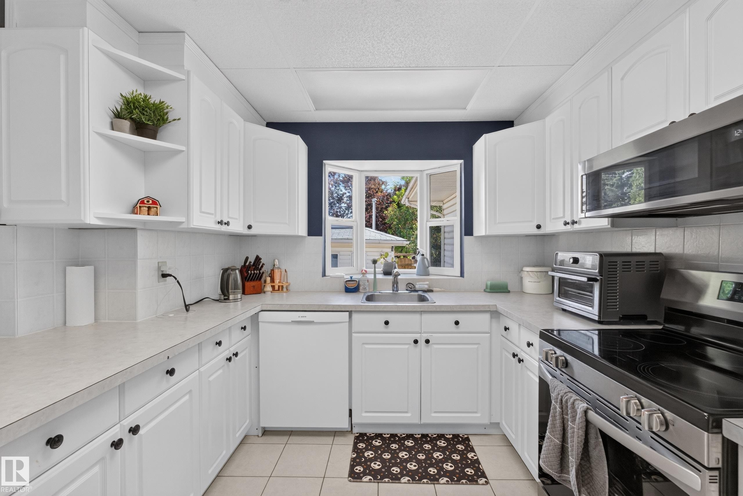 U-shaped kitchen featuring white cabinetry, a built-in stainless steel microwave, and an electric range - 11015 122 Street, Edmonton, AB