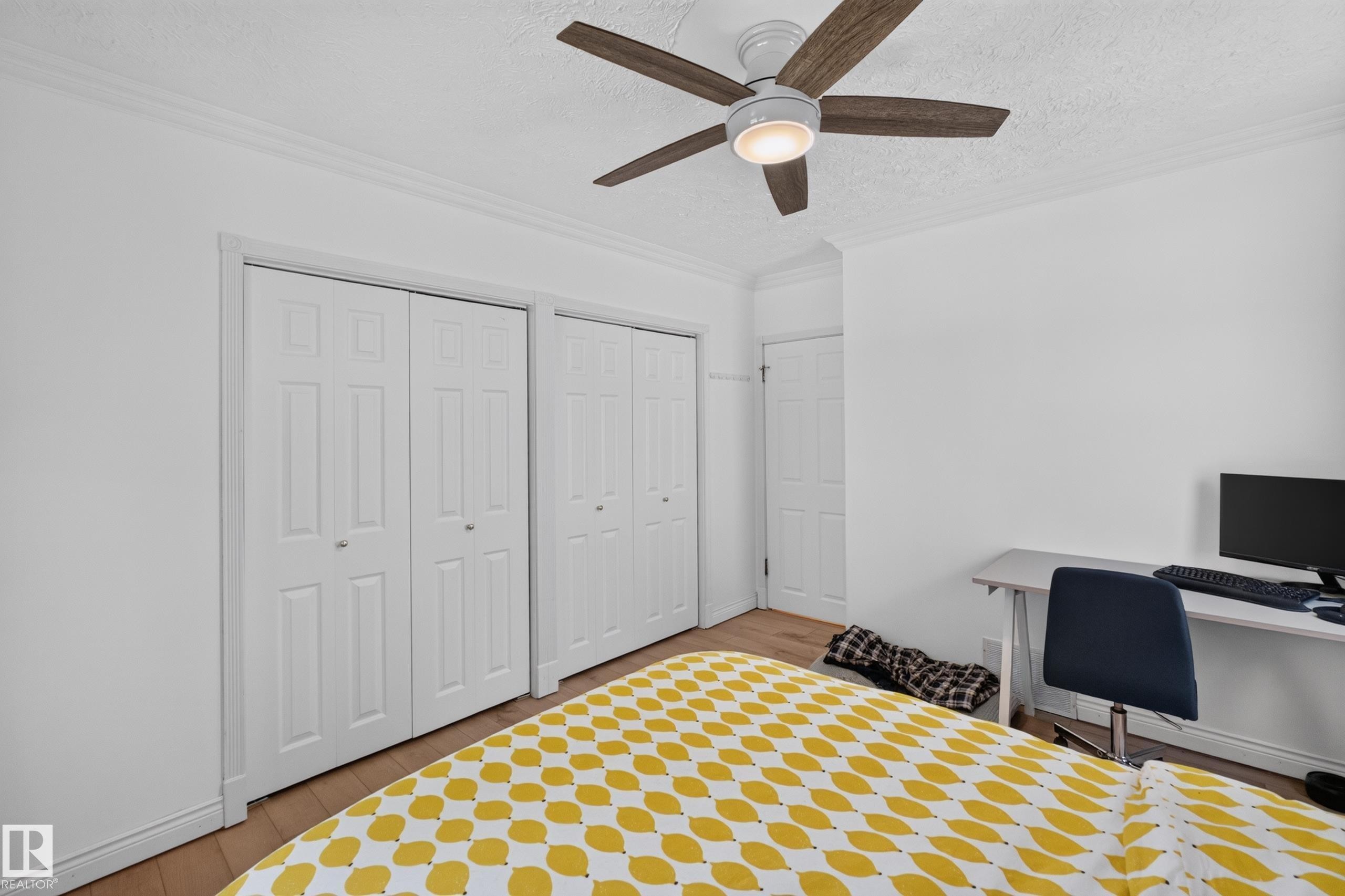 Room featuring wood-finish flooring, two sets of bi-fold closet doors, a ceiling fan with integrated lighting, and crown molding - 11015 122 Street, Edmonton, AB