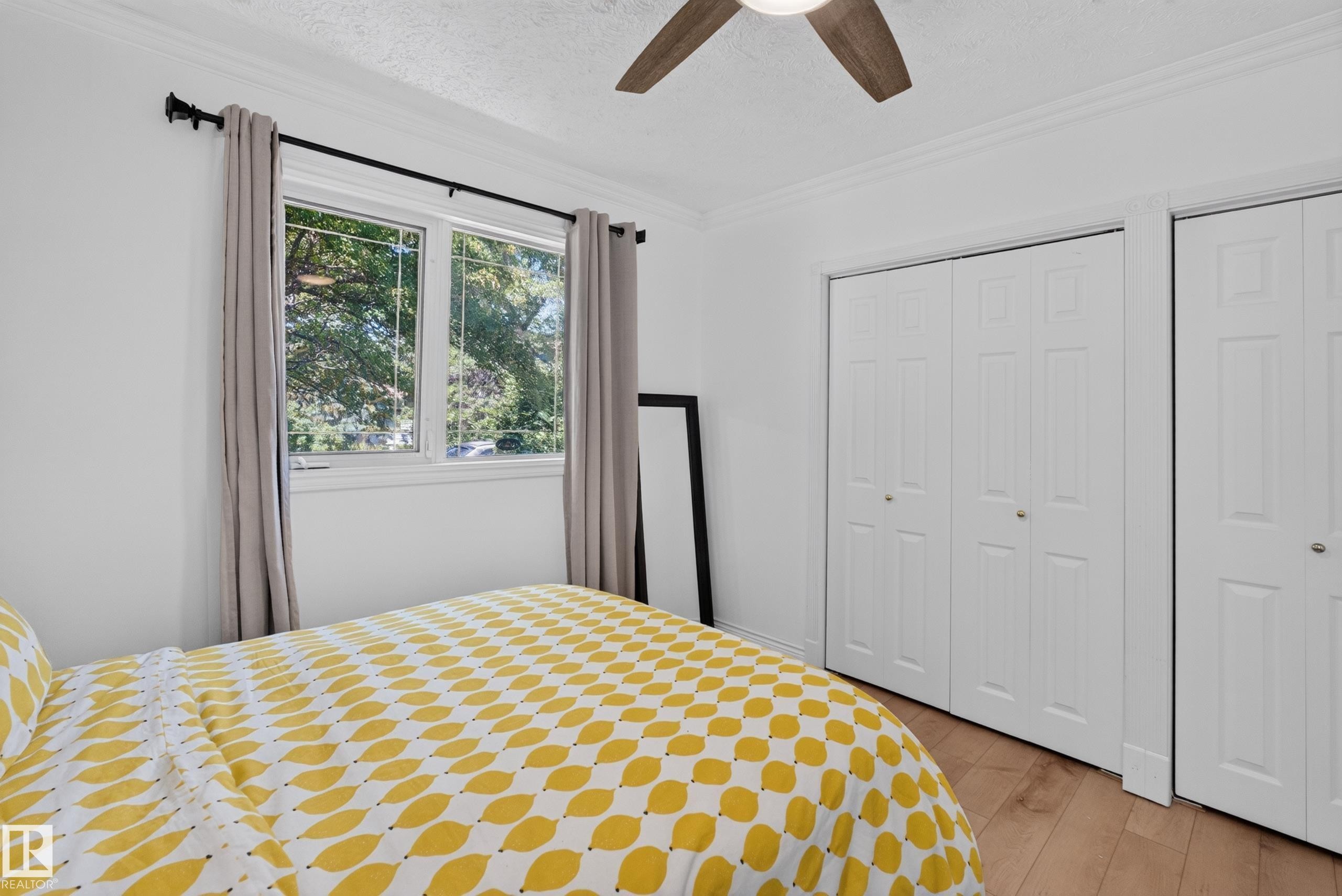 Bedroom featuring wood-finish flooring, a window with exterior tree-line scenery, and a ceiling fan with integrated lighting - 11015 122 Street, Edmonton, AB