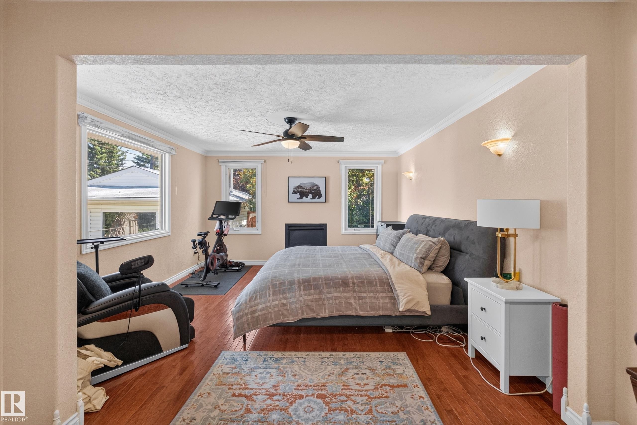 Hardwood-style flooring throughout this room, featuring multiple windows, crown molding, a ceiling fan with integrated lighting, and a built-in fireplace - 11015 122 Street, Edmonton, AB