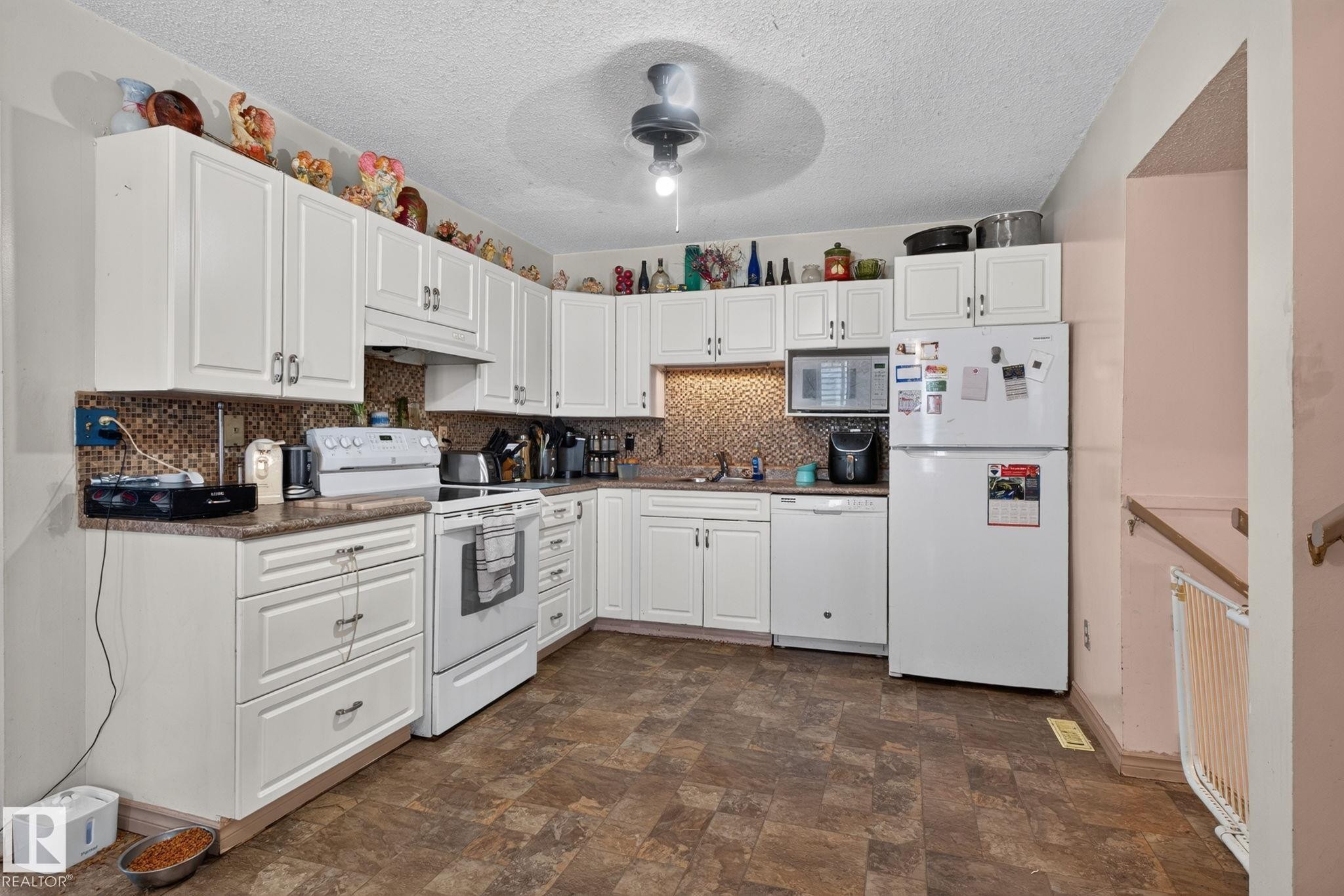 Well-appointed kitchen featuring extensive white cabinetry, a tiled backsplash, and durable patterned flooring - 8316 157 Avenue, Edmonton, AB
