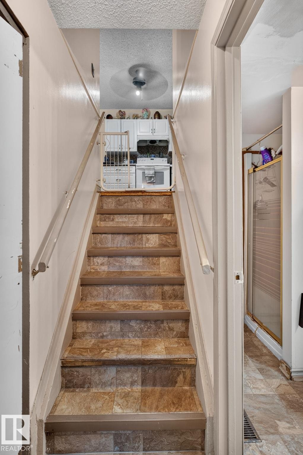 Staircase with patterned flooring, white wall-mounted handrails, and a ceiling fan visible at the landing - 8316 157 Avenue, Edmonton, AB
