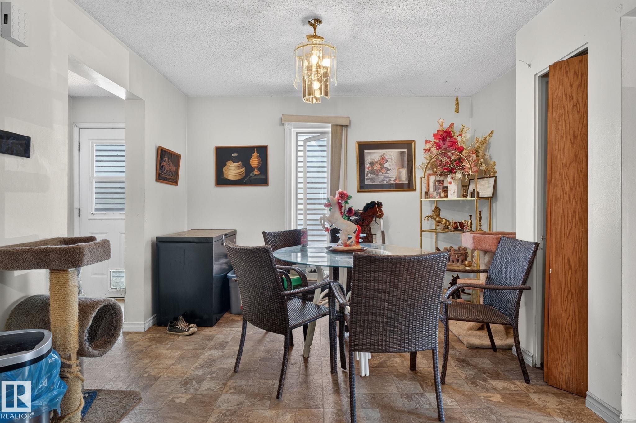 Dining area featuring a contemporary chandelier, textured ceiling, and wood-finish flooring - 8316 157 Avenue, Edmonton, AB