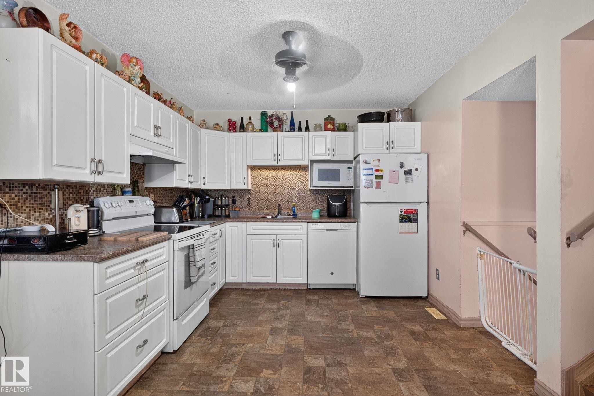 Kitchen featuring white cabinetry, mosaic tile backsplash, brown-toned flooring, and a ceiling fan with integrated lighting - 8316 157 Avenue, Edmonton, AB