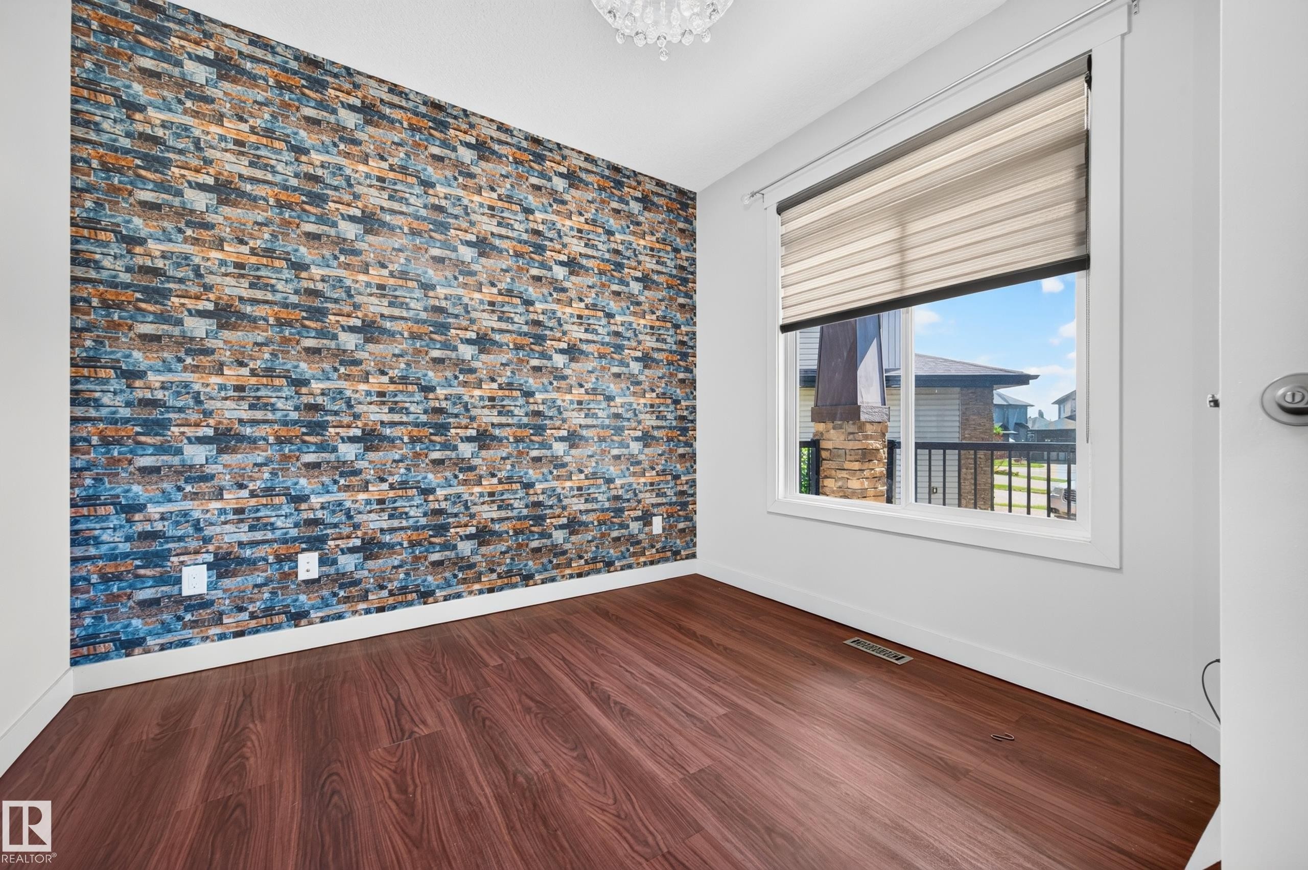 Feature wall with stacked stone-look finish, wood-finish flooring, white baseboards, window with blinds, and ceiling-mounted light fixture - 1512 Cunningham Cape, Edmonton, AB