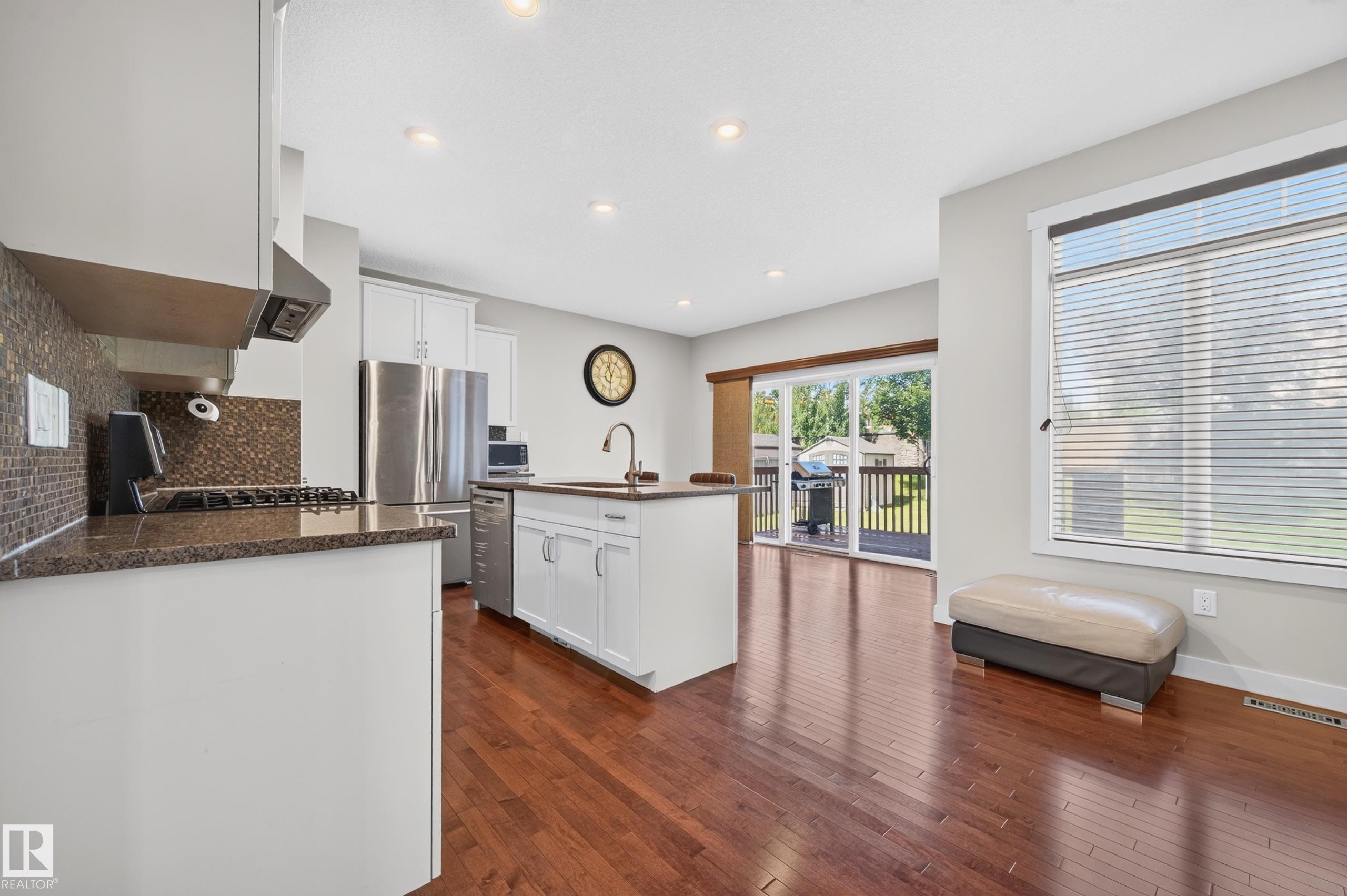 Open-concept kitchen with wood-finish flooring, white cabinetry, dark stone countertops, and a full stainless steel appliance package - 1512 Cunningham Cape, Edmonton, AB