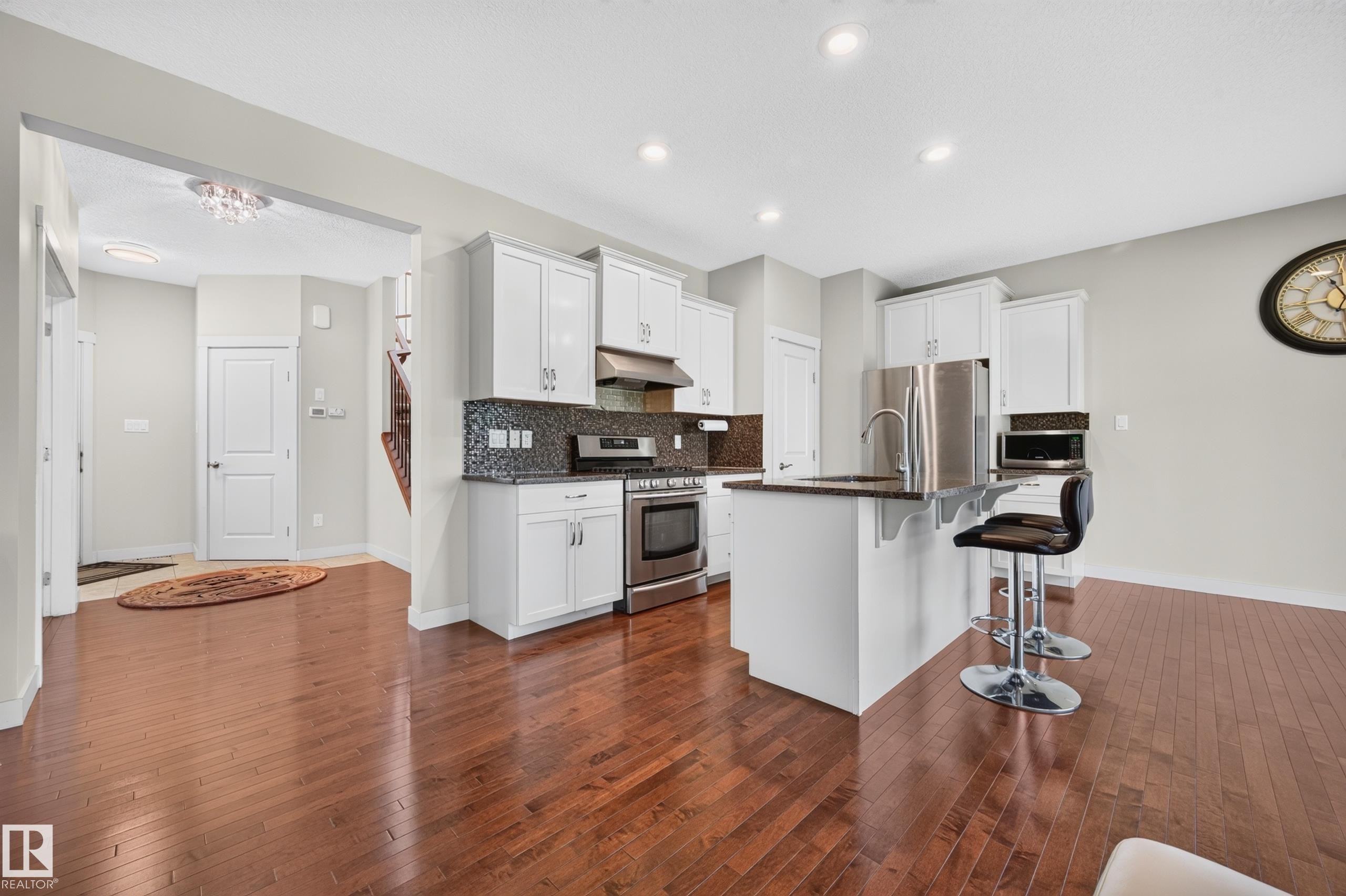 Open-concept kitchen featuring white cabinetry, dark stone countertops, stainless steel appliances, a mosaic tile backsplash, and wood-finish flooring - 1512 Cunningham Cape, Edmonton, AB