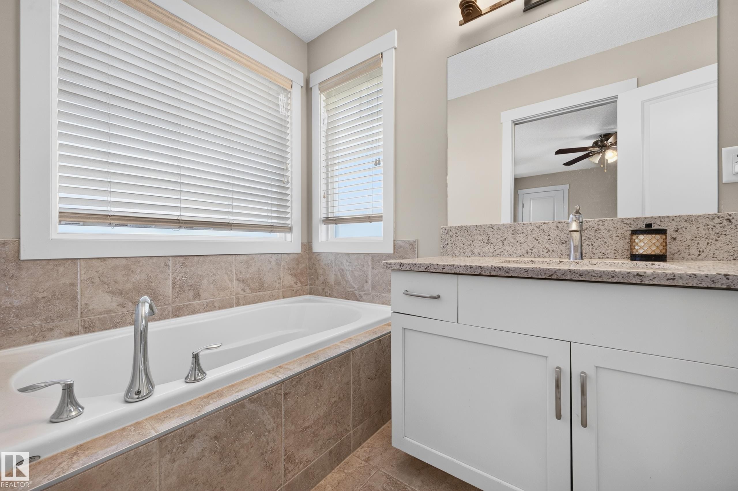 Integrated bathtub with deck-mounted chrome fixtures, surrounded by neutral-toned tiled walls - 1512 Cunningham Cape, Edmonton, AB