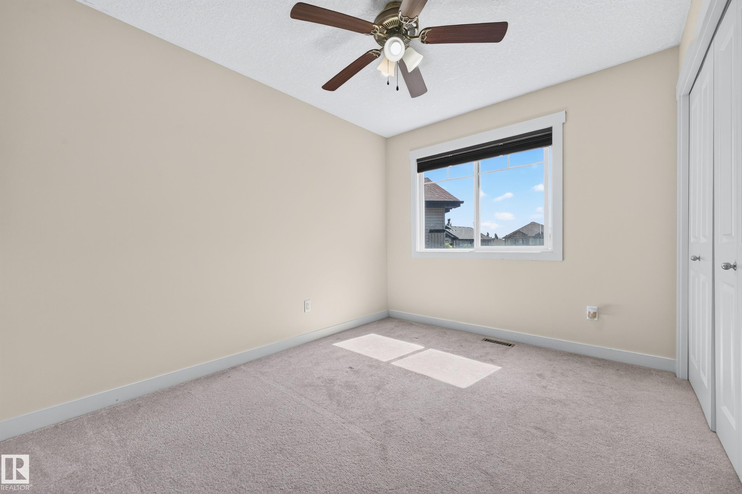 Neutral-toned room featuring a single window, a ceiling fan with integrated lighting, and light-colored carpeting - 1512 Cunningham Cape, Edmonton, AB