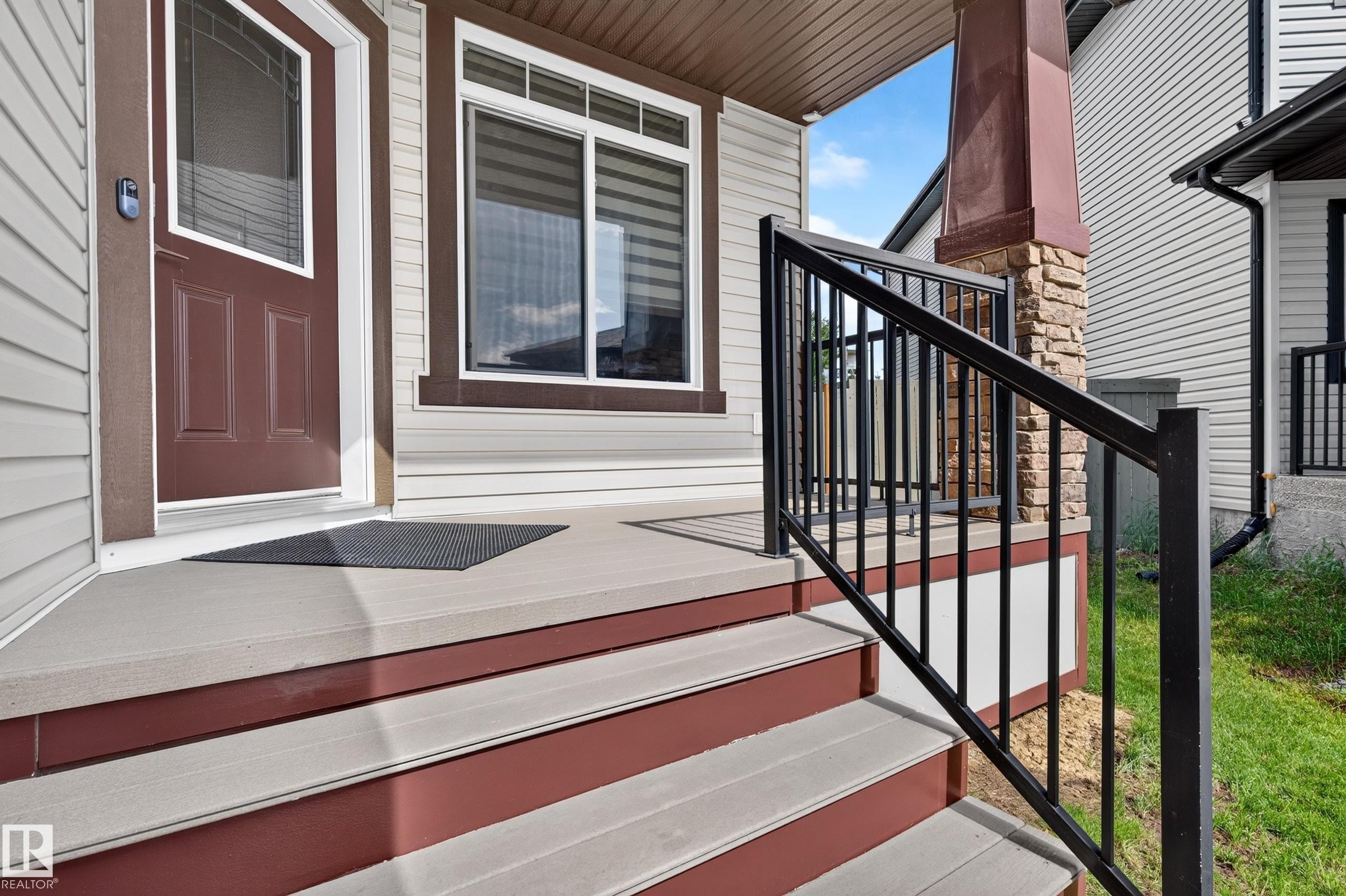Covered front porch featuring durable composite decking, contrasting dark brown trim, and a robust black metal railing - 1512 Cunningham Cape, Edmonton, AB