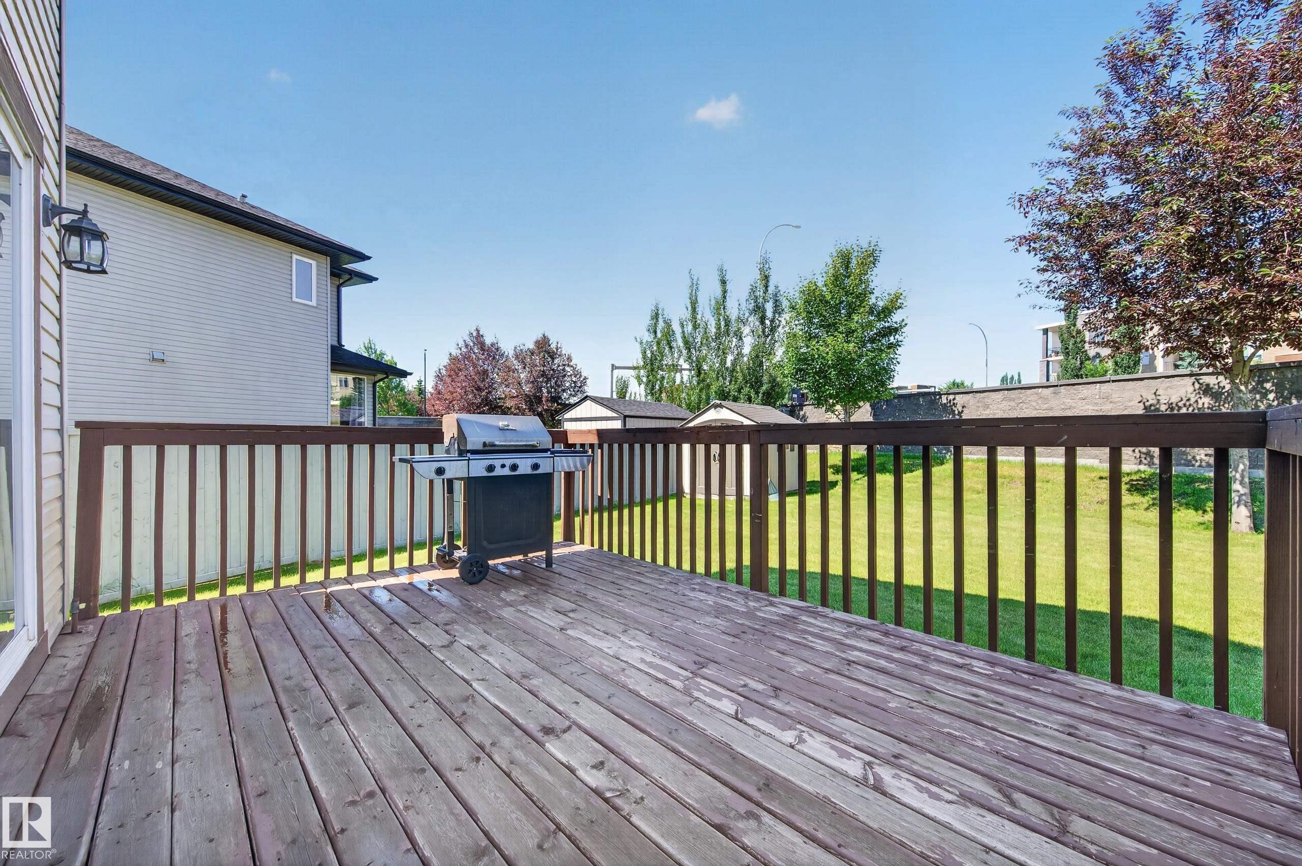 Expansive outdoor wood deck with dark-stained railing, offering direct access to the grassy yard - 1512 Cunningham Cape, Edmonton, AB