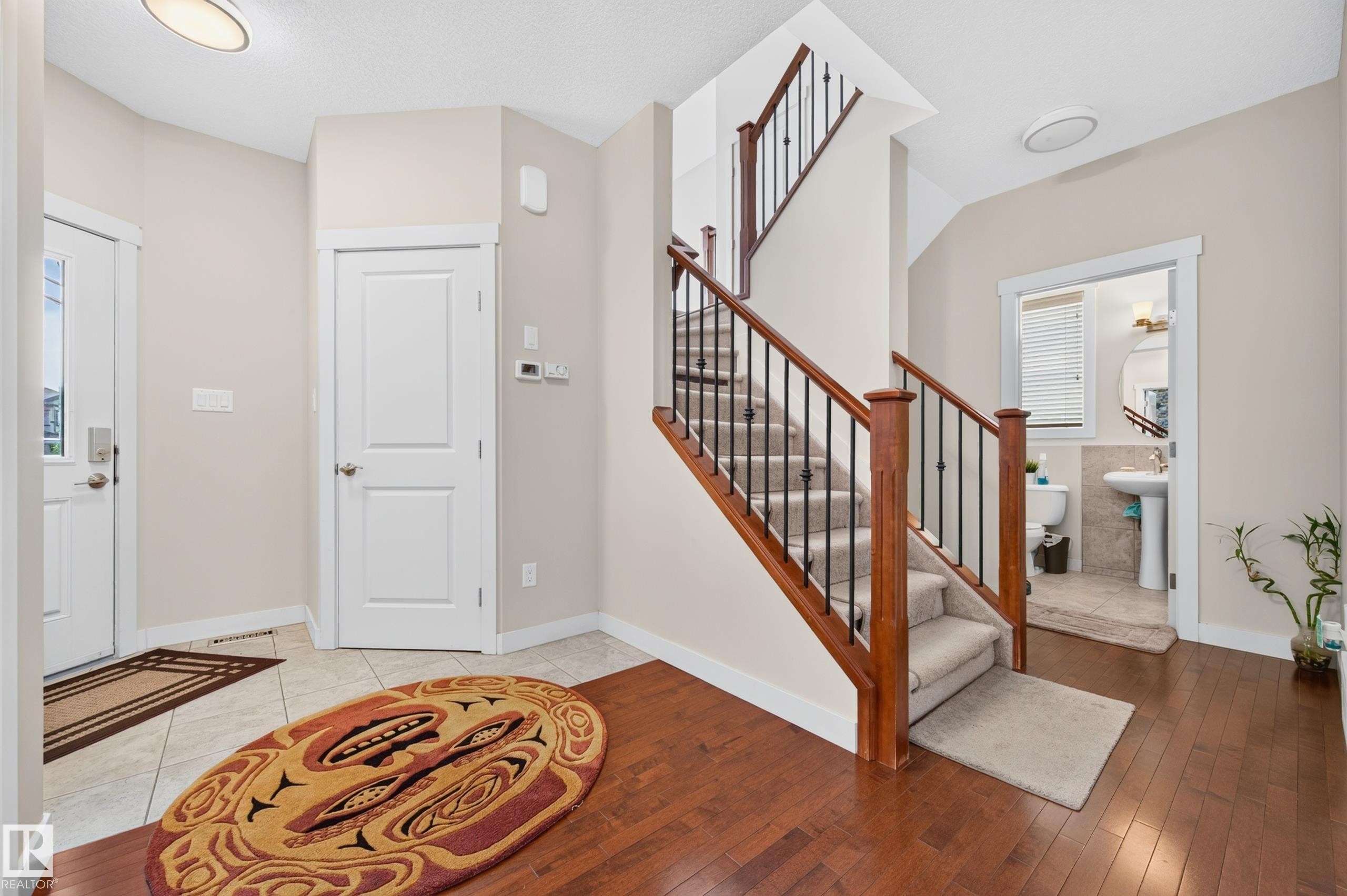 Inviting entryway featuring wood-finish flooring, a carpeted staircase with wood and metal railings, and a tiled landing - 1512 Cunningham Cape, Edmonton, AB