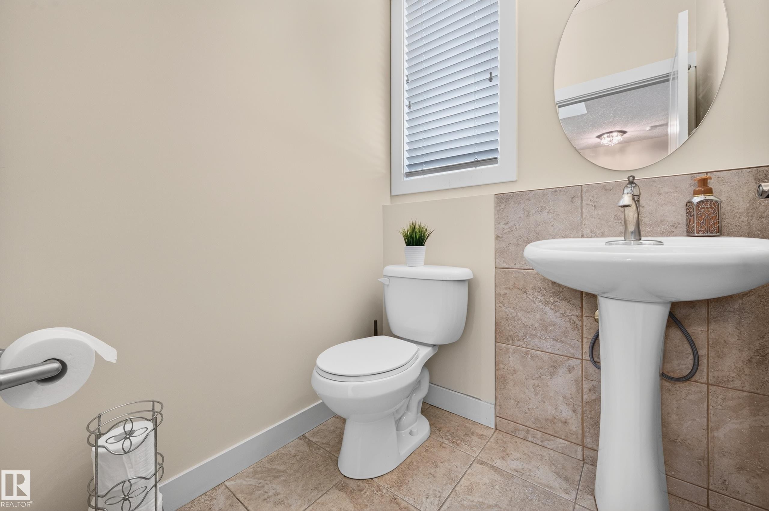 Pedestal sink with chrome faucet, complemented by a round wall mirror - 1512 Cunningham Cape, Edmonton, AB