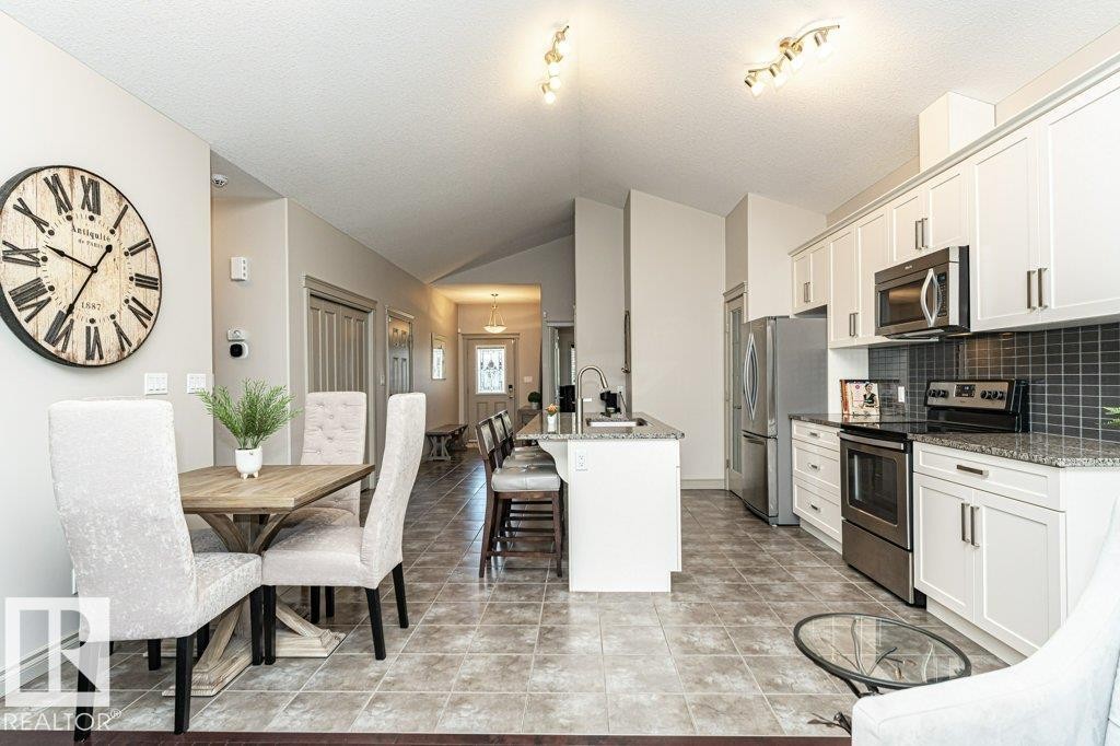 Kitchen featuring white cabinetry, stainless steel appliances, granite countertops, and a subway tile backsplash - 15 175 Mcconachie Drive, Edmonton, AB