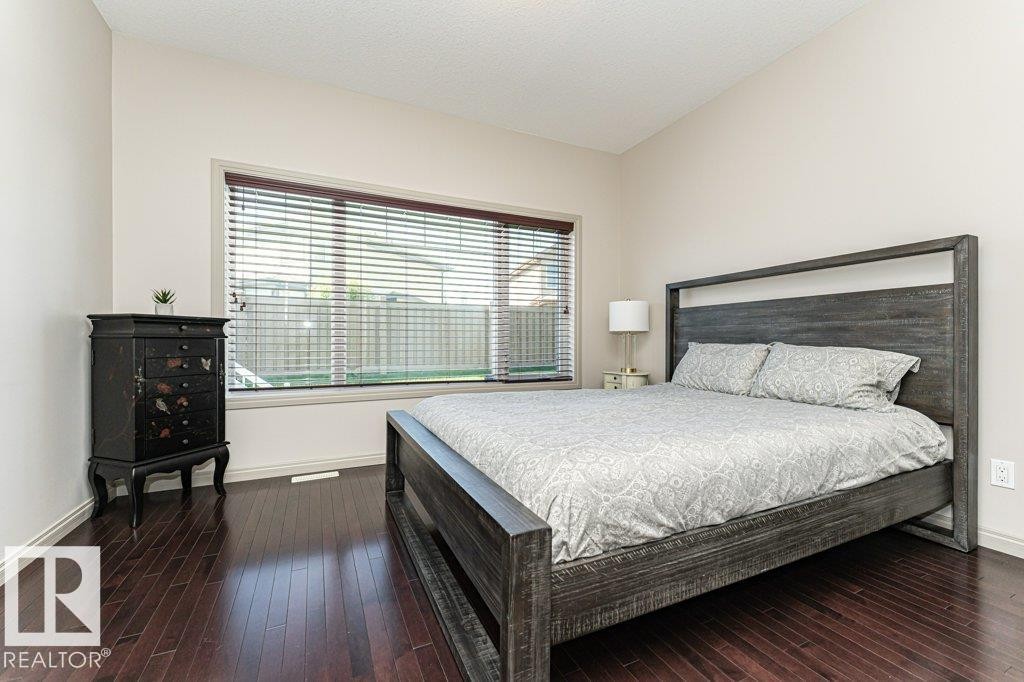 Spacious room featuring rich wood-finish flooring, a large window with horizontal blinds, and neutral painted walls - 15 175 Mcconachie Drive, Edmonton, AB