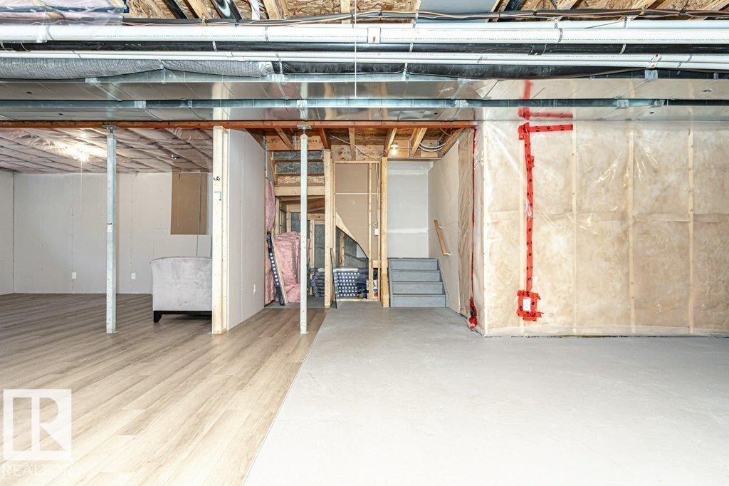 Spacious lower level featuring wood-finish flooring, exposed ceiling joists and ductwork, a partially finished area with white panel walls, and a concrete floor area - 15 175 Mcconachie Drive, Edmonton, AB