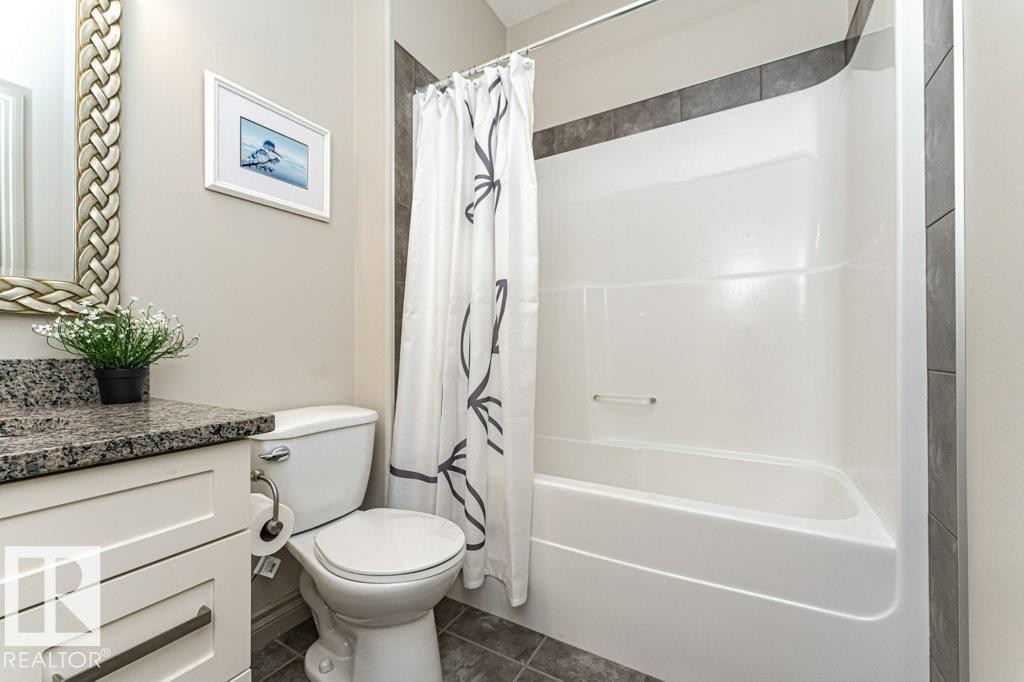 Bathroom featuring a white vanity with a dark speckled countertop, a toilet, and a white tub with a shower curtain - 15 175 Mcconachie Drive, Edmonton, AB